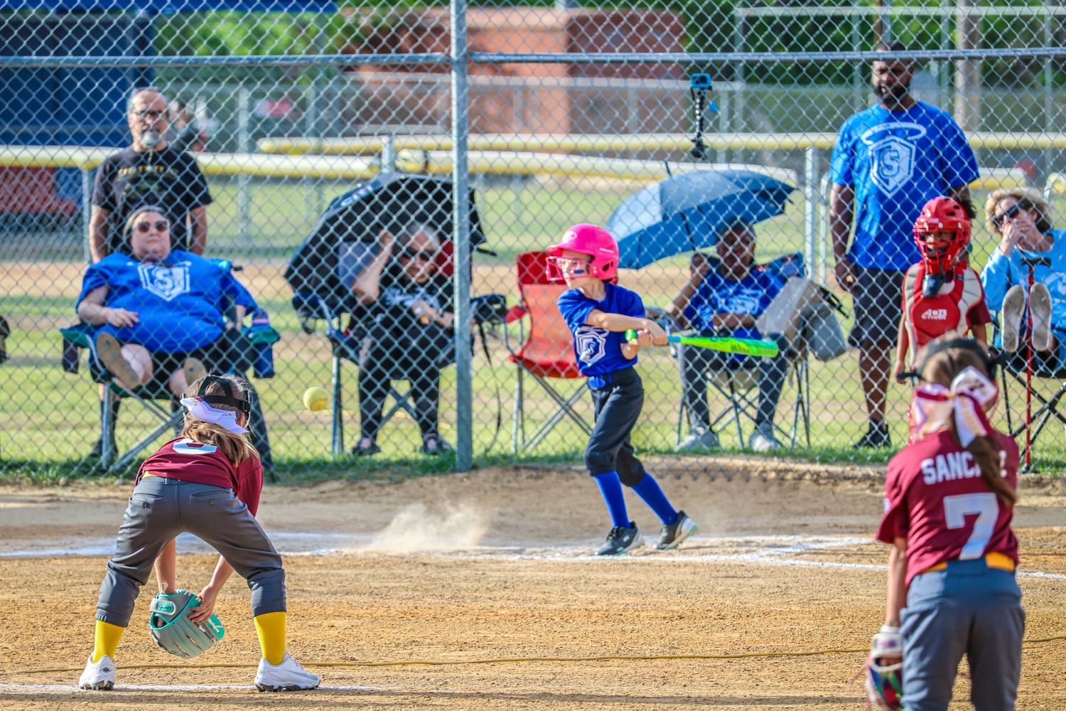 Youth softball players compete during a game as spectators watch from behind the fence.