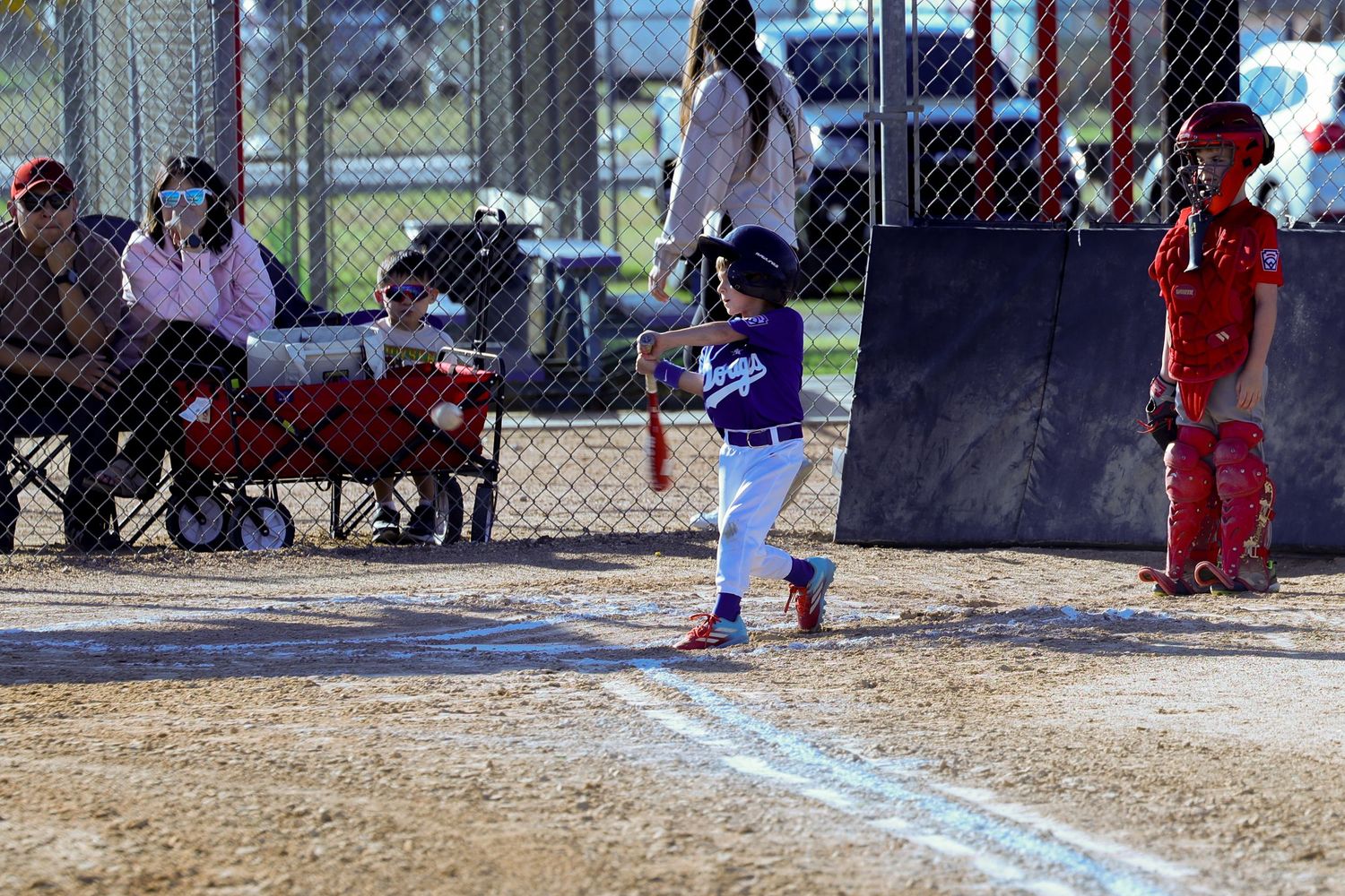 Young baseball player in purple uniform swinging bat at home plate during a youth league game.