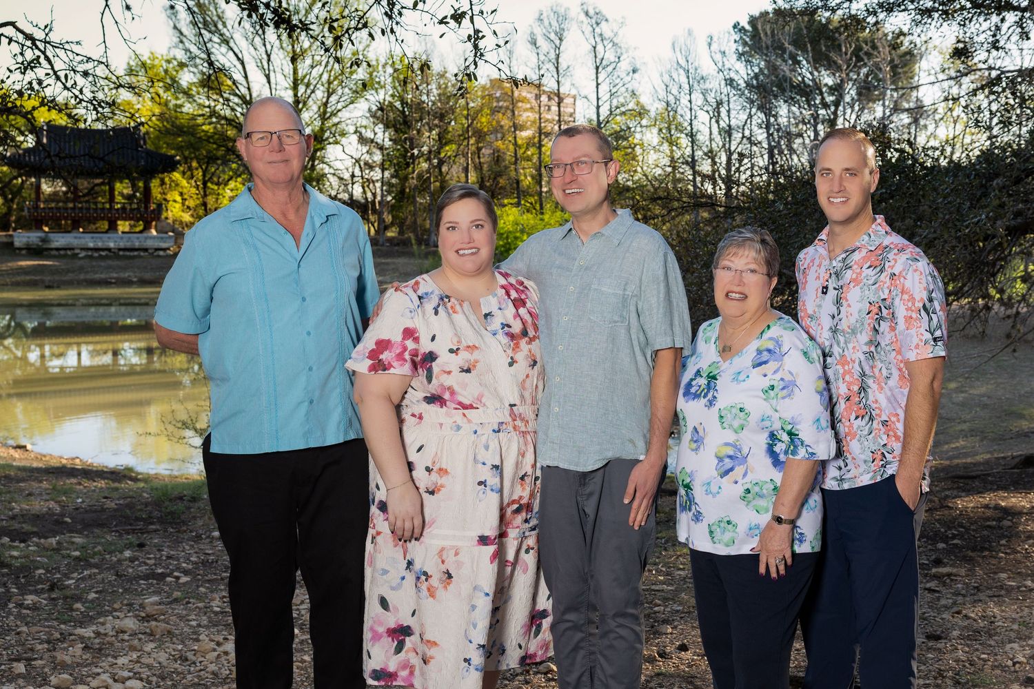 A group of five people, two men and three women, stand together outdoors in a natural setting.