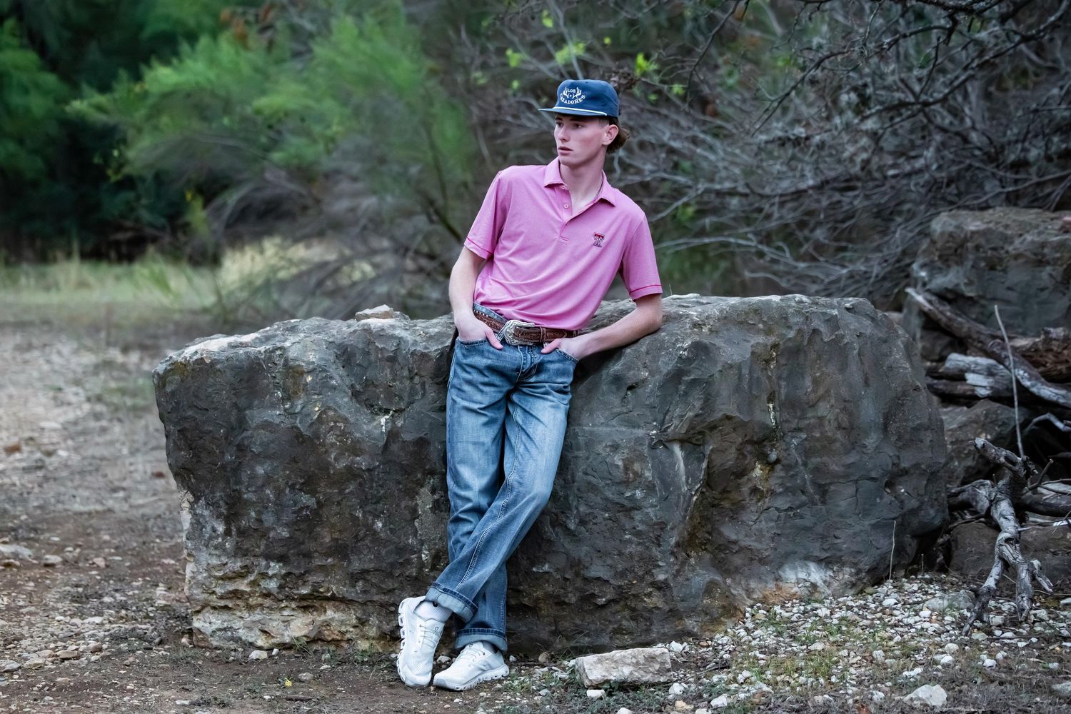 A person in casual attire sits on a rocky outcrop near a wooded area in natural lighting.