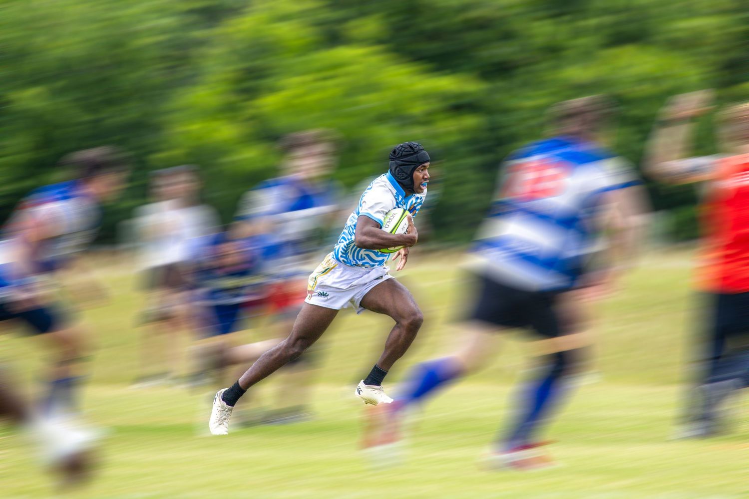 A rugby player sprints at full speed during a match, captured with motion blur effect on a green field.