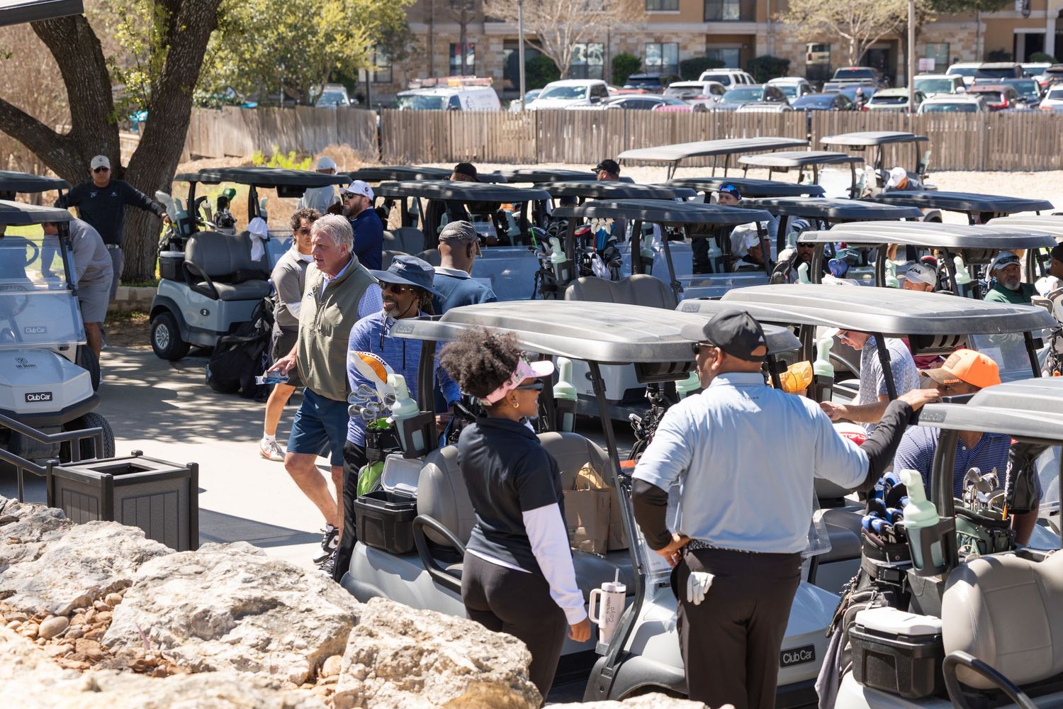 Crowded golf cart parking area at a golf tournament with players and staff gathered on a sunny day.