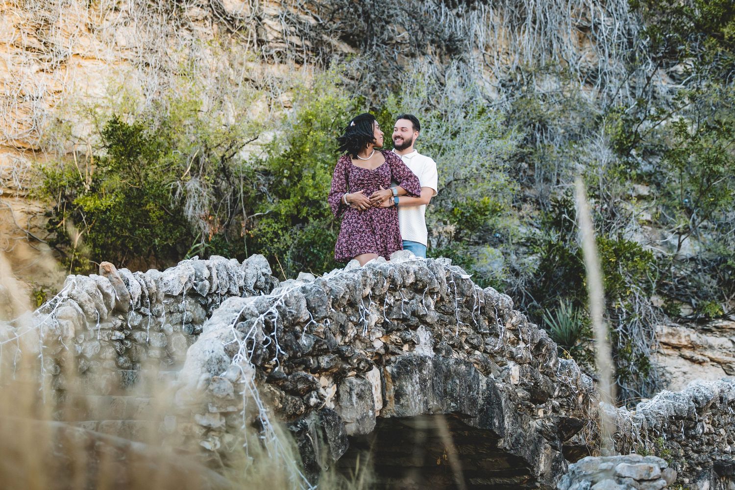 People exploring a scenic rocky cliff face with waterfalls and lush vegetation in a natural outdoor setting.