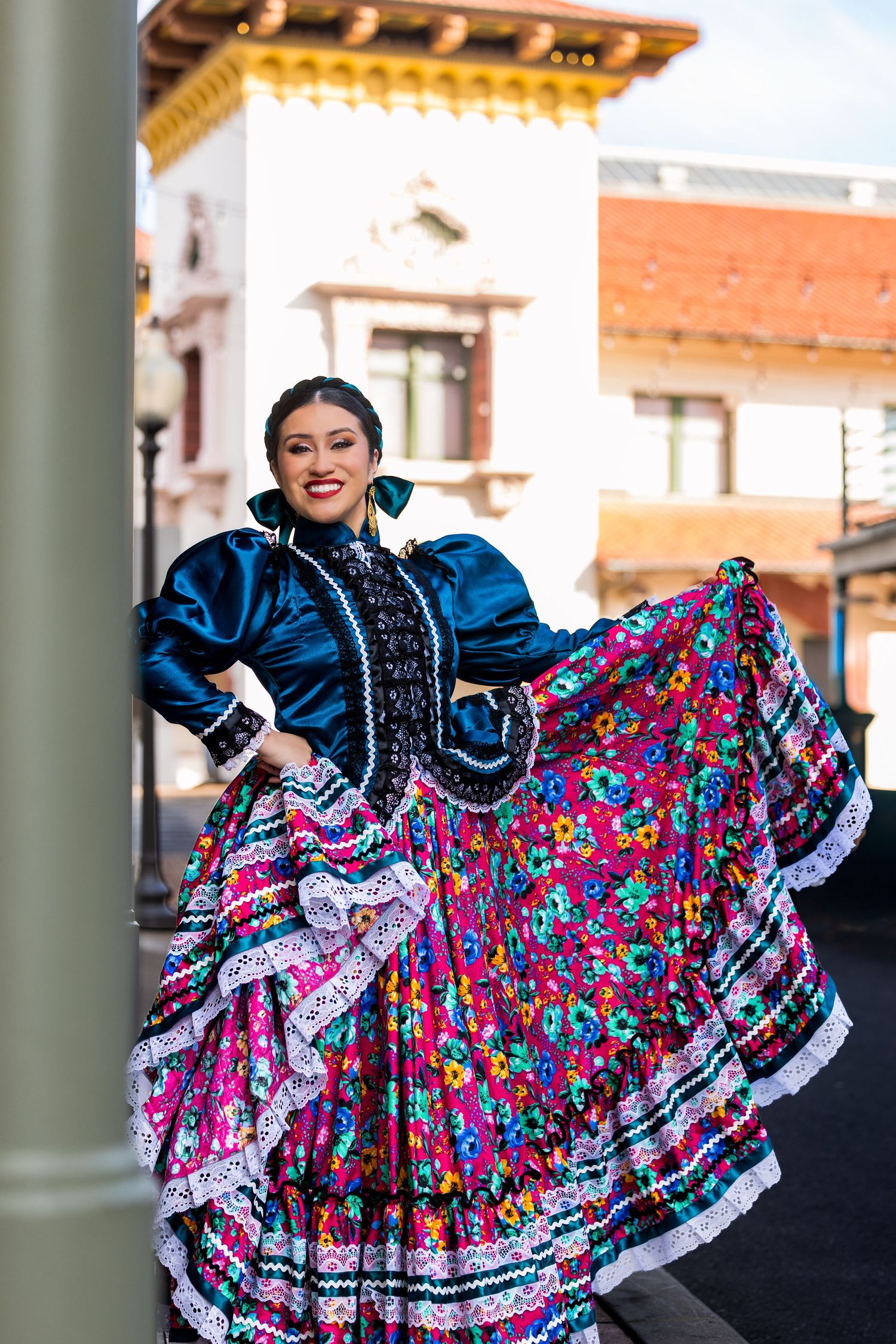 A dancer in a vibrant blue and floral traditional Mexican folklorico dress performs a spinning movement on stage.