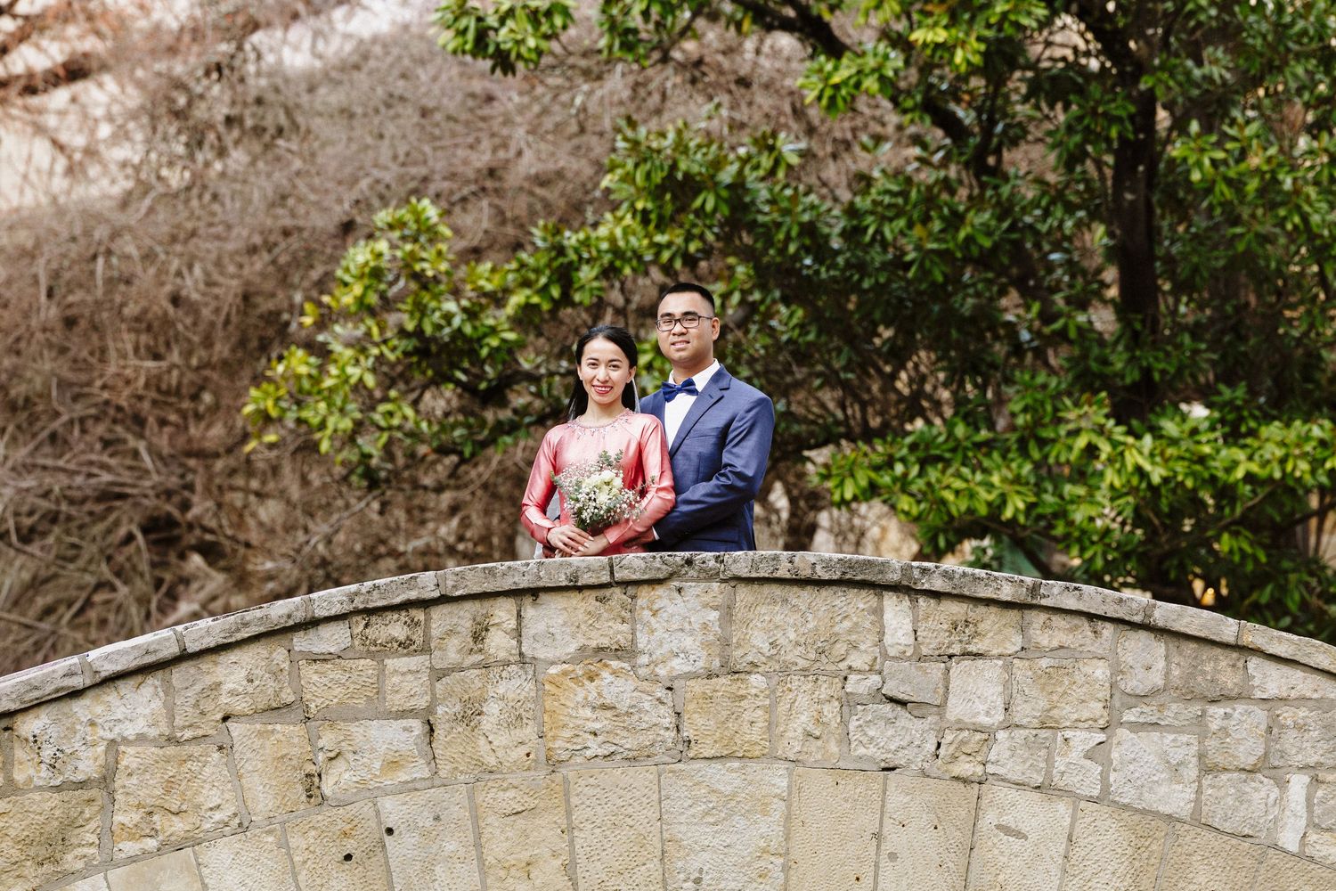 A couple shares a romantic moment on a stone bridge surrounded by lush greenery during an engagement photoshoot.