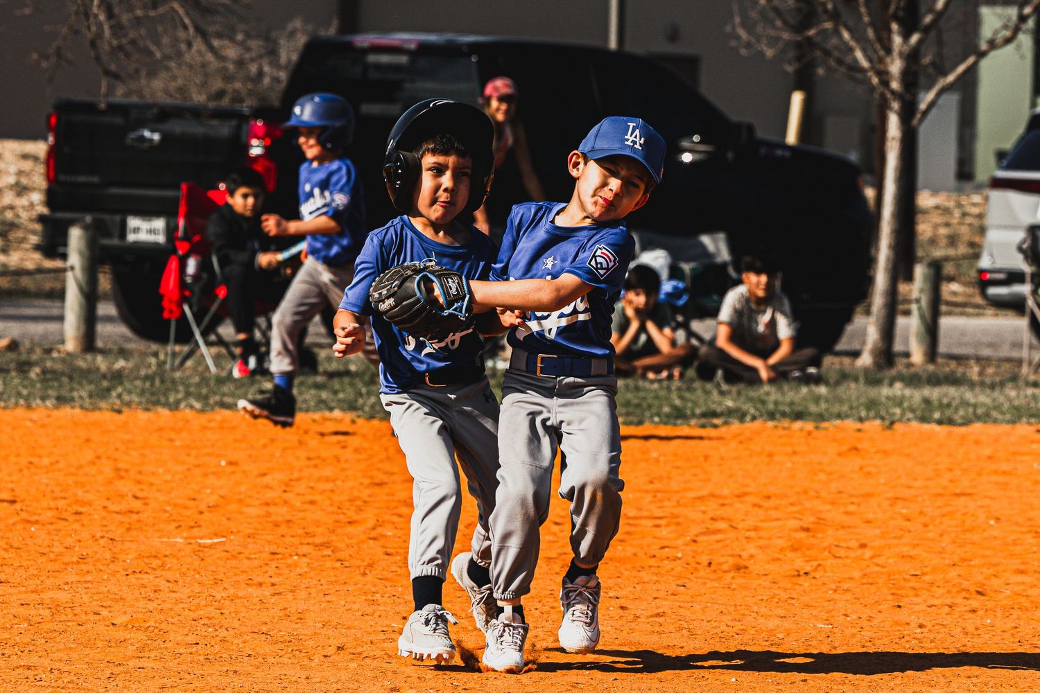 Two young boys in blue baseball uniforms playing on an orange dirt field during a little league game.