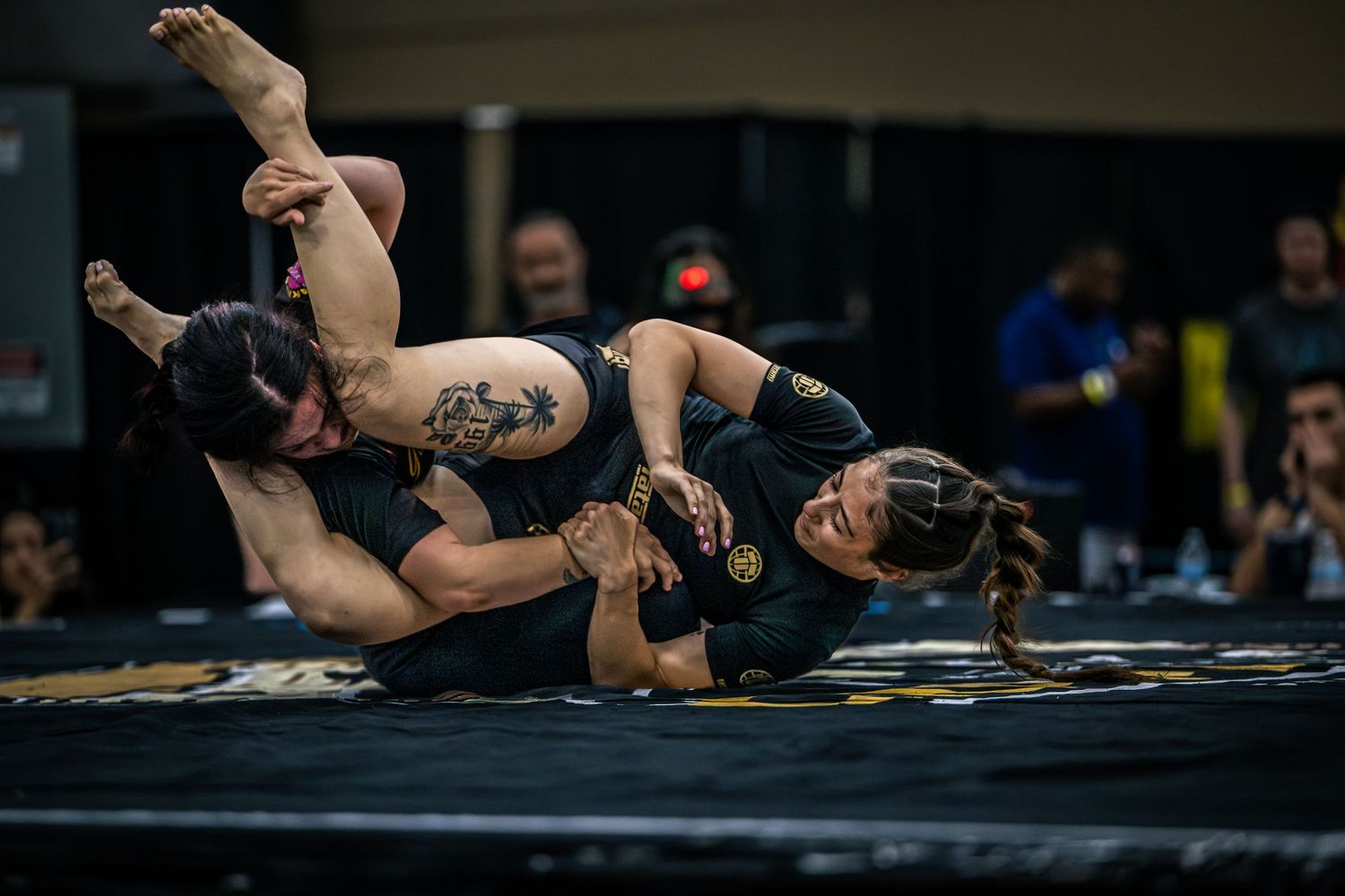 Two female MMA fighters grappling on the mat during a competitive submission wrestling match.