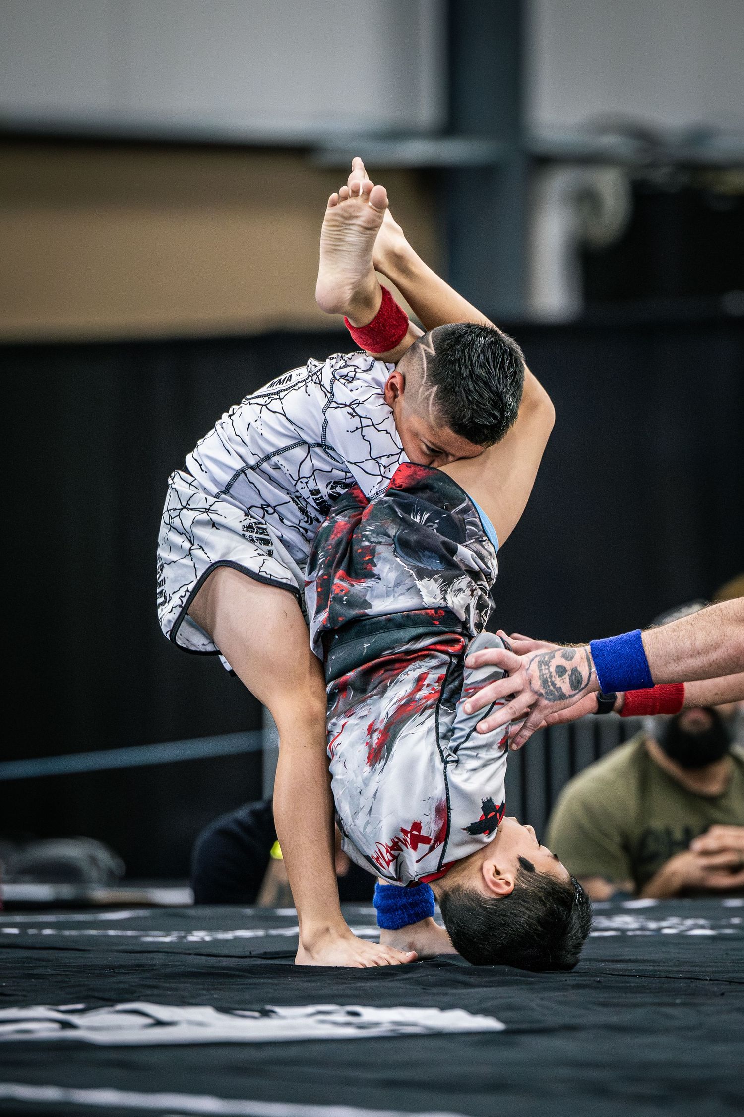 Two wrestlers compete in a grappling match, one athlete performing a dramatic flip technique on a mat.