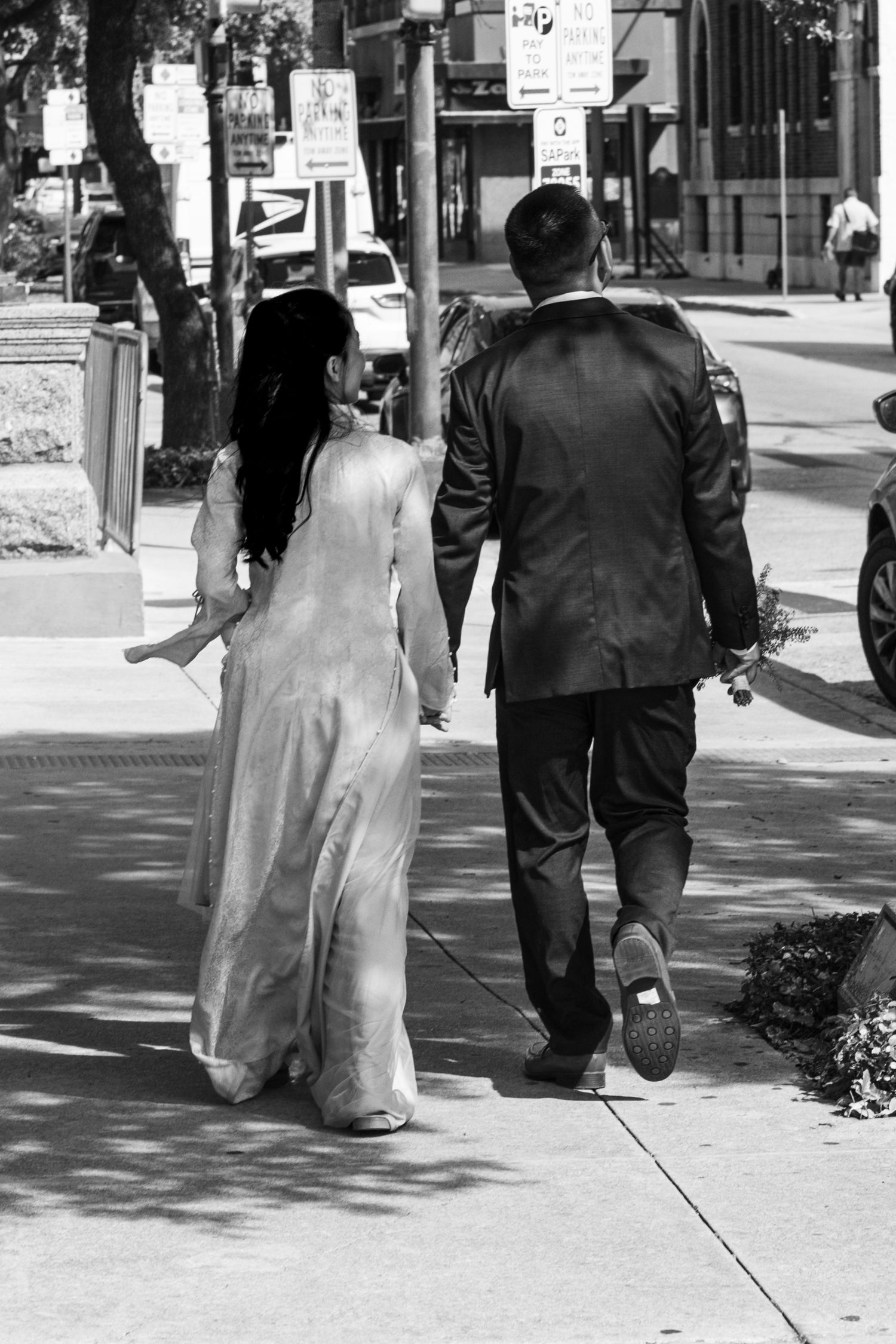 A black and white sequence of a bride and groom walking down a city sidewalk together.