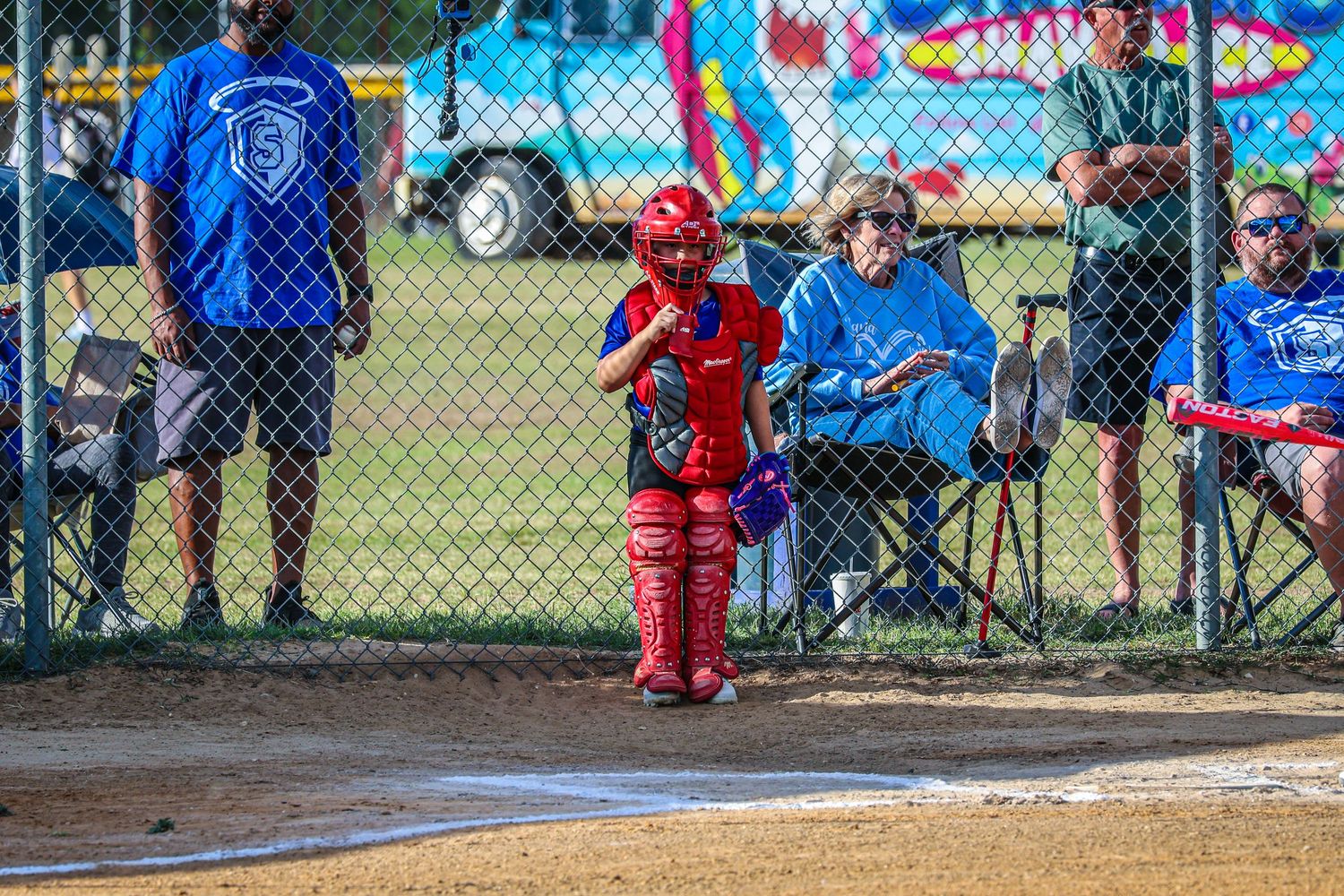 Young youth softball catcher in full red gear standing near home plate during a game.