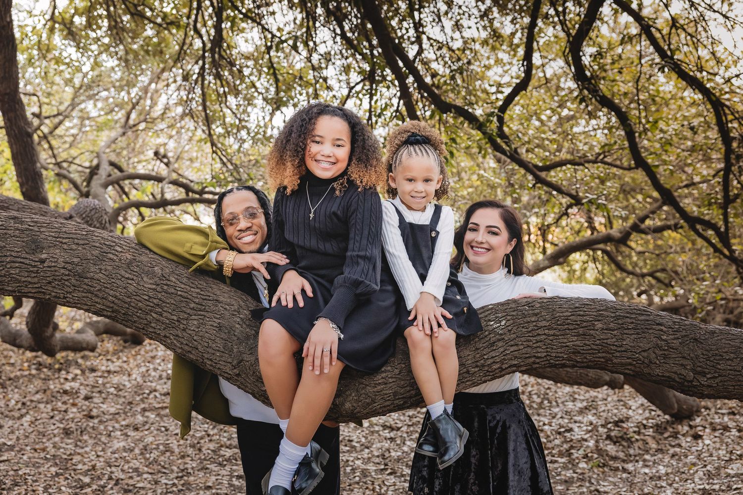 A family poses together in autumn foliage wearing coordinated black and white outfits for outdoor portraits.