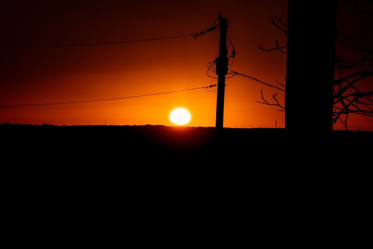 Orange sunset horizon with power lines and poles creating dark silhouettes.