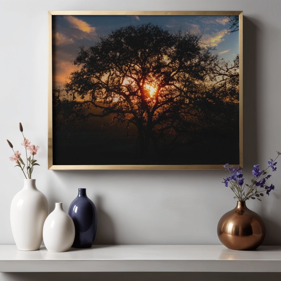 Sunset silhouettes a tree through panoramic wall art displayed above white and blue ceramic vases on wooden furniture.