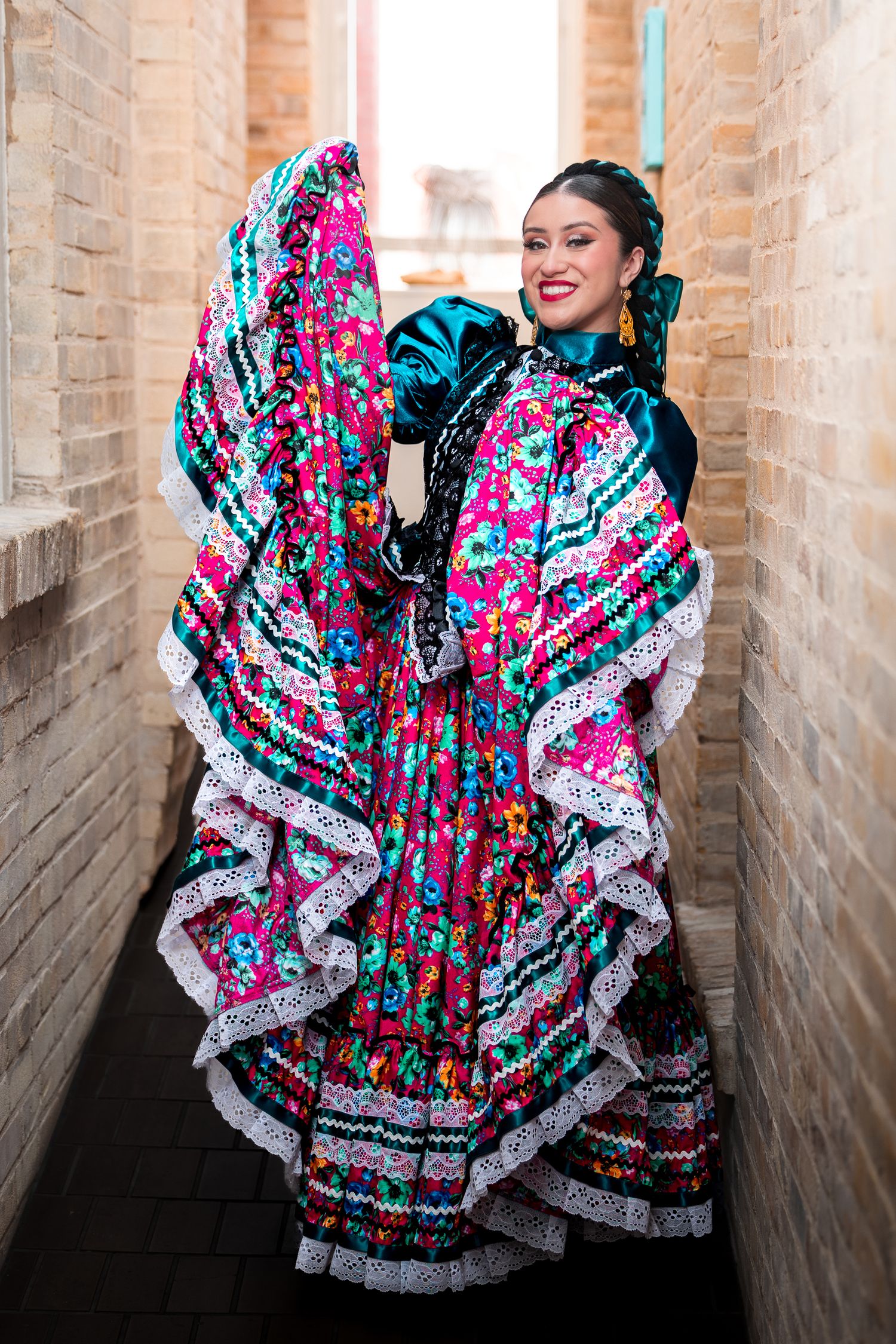 Colorful Mexican folk dance dress with vibrant pink and turquoise floral patterns twirls in a brick hallway.