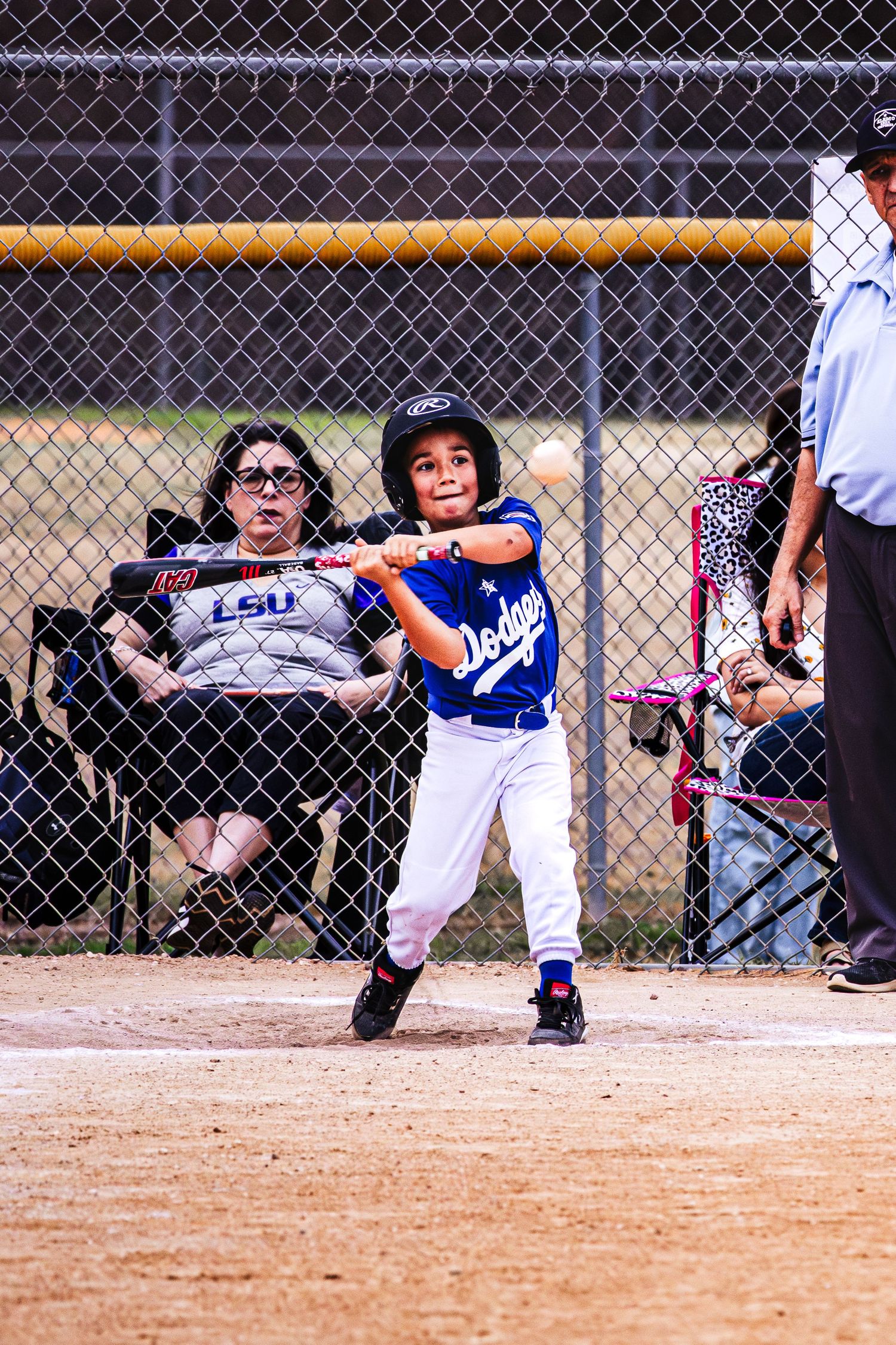 Young boy in Dodgers uniform swinging baseball bat at youth league game with umpire and spectator watching.