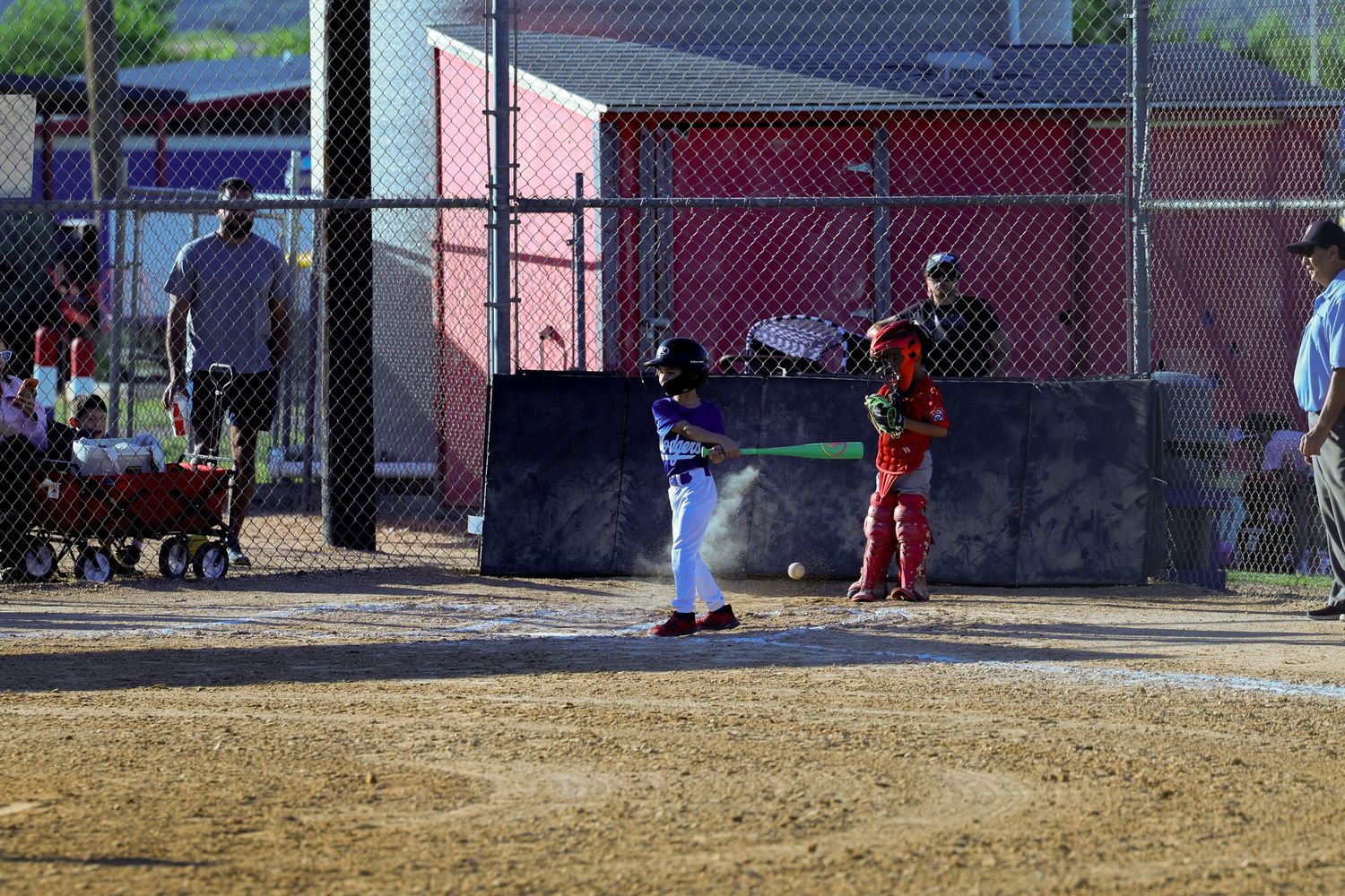 Young baseball player batting during a youth league game with catcher and umpire behind home plate on a dirt field.