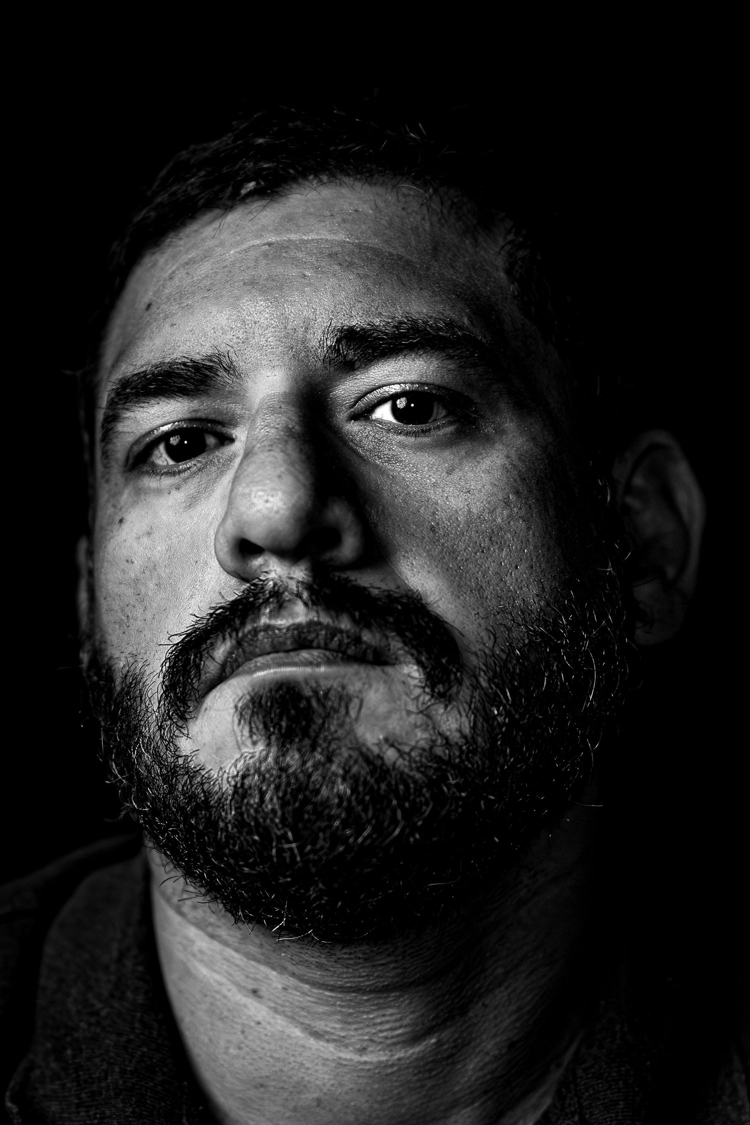 Black and white portrait of a bearded man with a serious expression against a dark background.