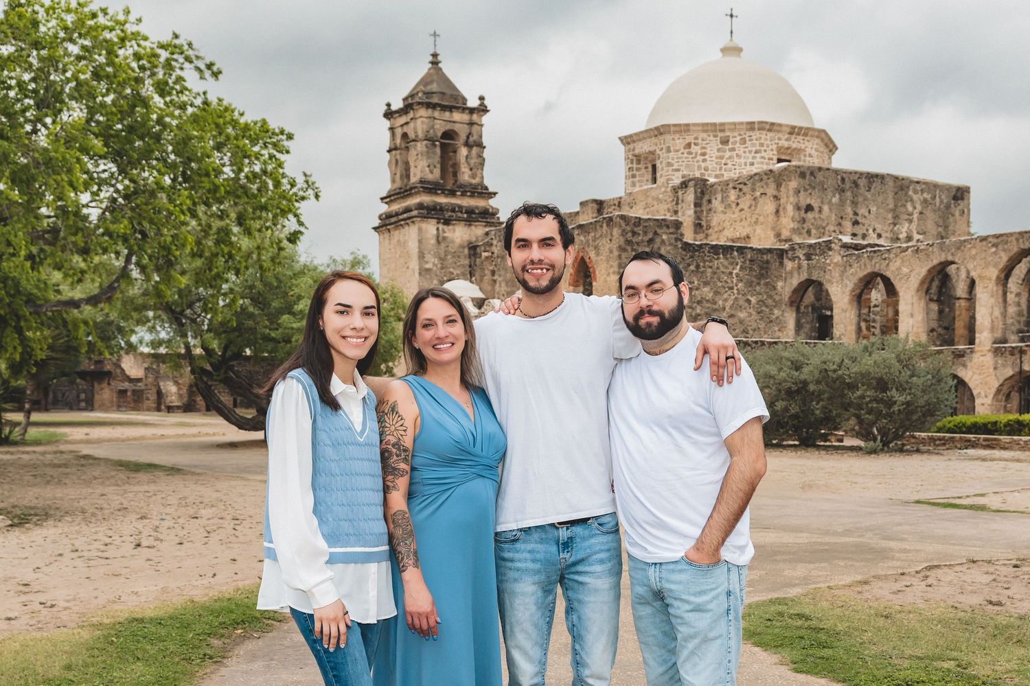 Four smiling friends pose together outdoors in front of a historic stone church in San Antonio, Texas.