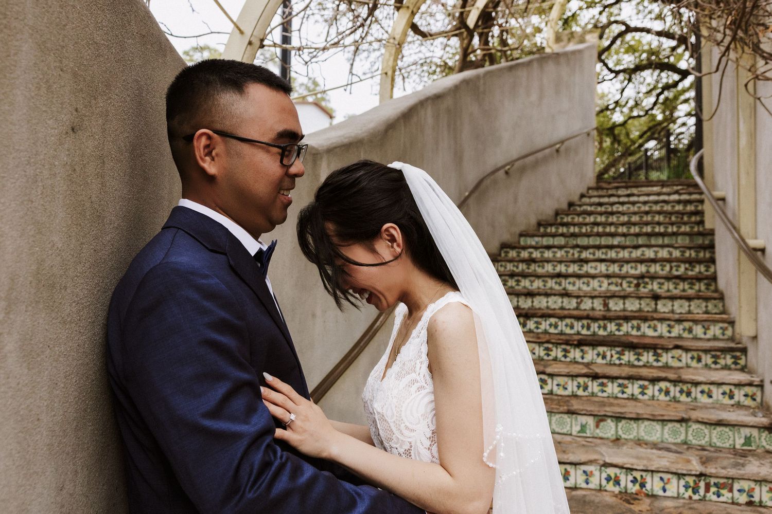 A romantic wedding couple embraces on an elegant stone staircase surrounded by autumn trees.