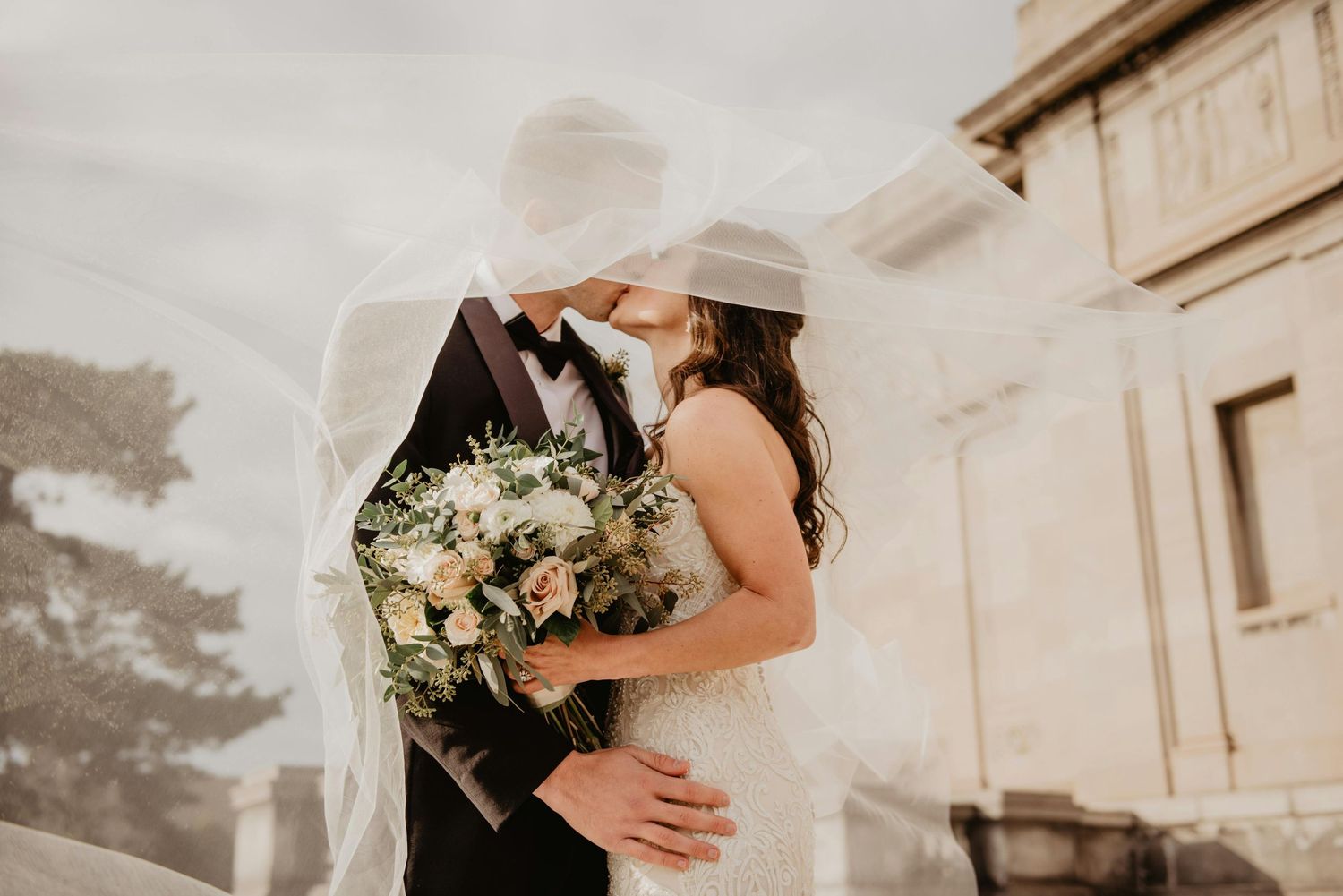 Elegant wedding couple embraces in a romantic outdoor setting with soft natural lighting.