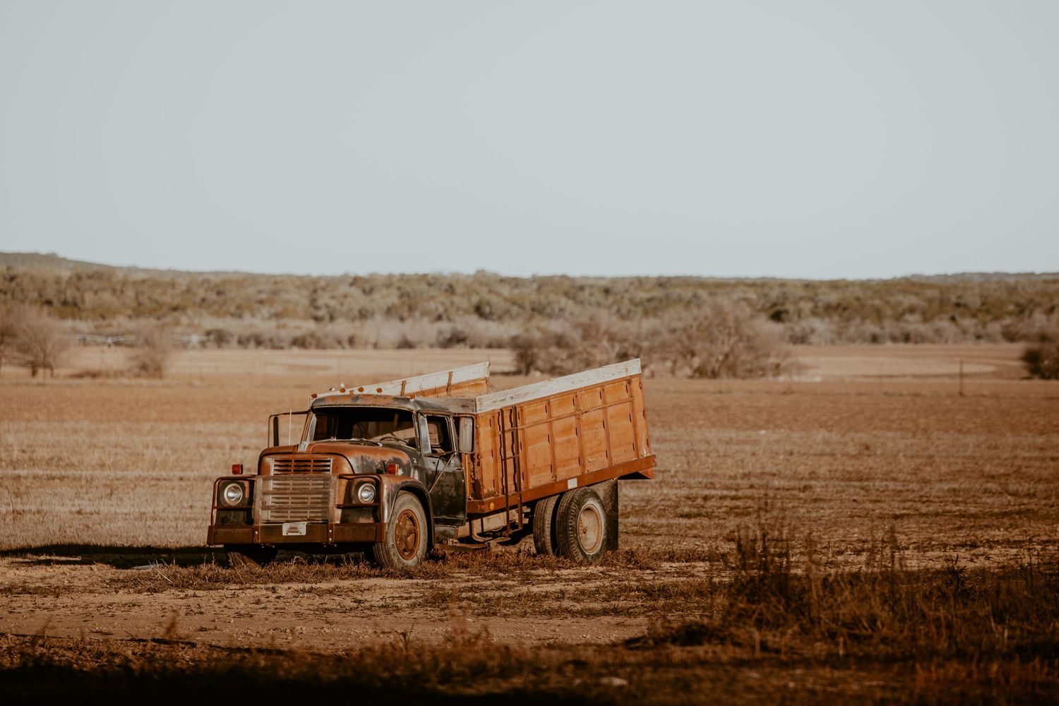 Vintage farm equipment sits abandoned on a dusty desert plain.