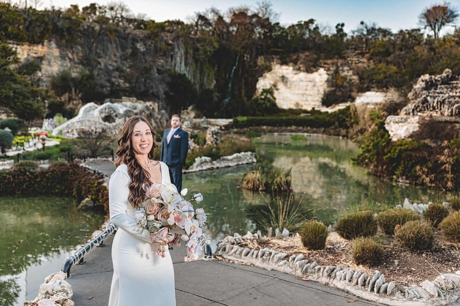 A couple poses together on rustic stone steps surrounded by lush greenery and natural landscaping.