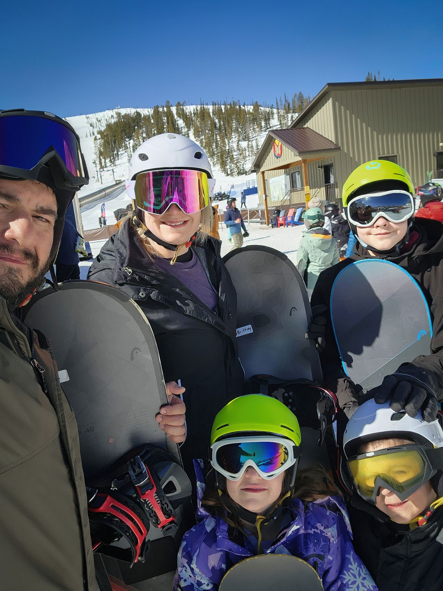 A group of skiers and snowboarders gather together on a sunny winter day at a snow-covered mountain resort.