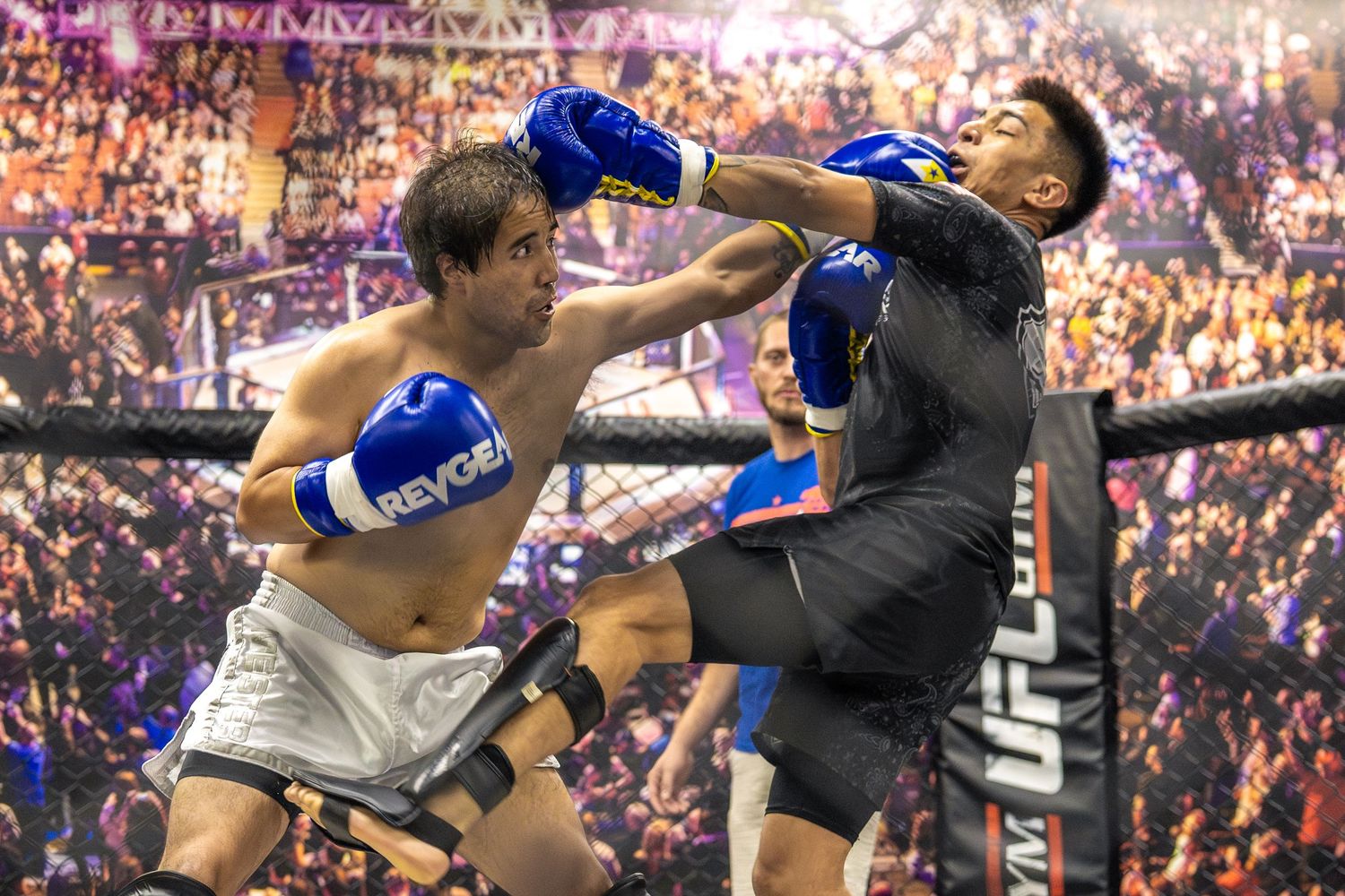 Two fighters exchanging strikes in a UFC Gym boxing match, one landing a punch while wearing blue gloves.
