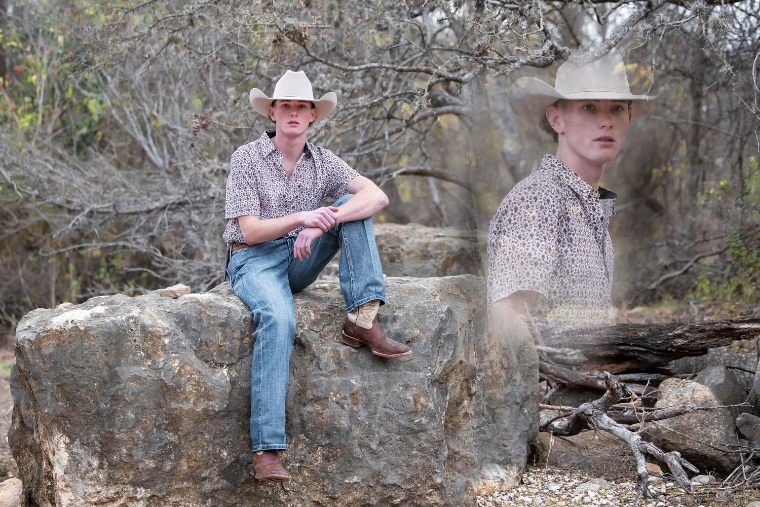 A person in a cowboy hat sits on a rustic stone wall while holding a cup in a natural outdoor setting.
