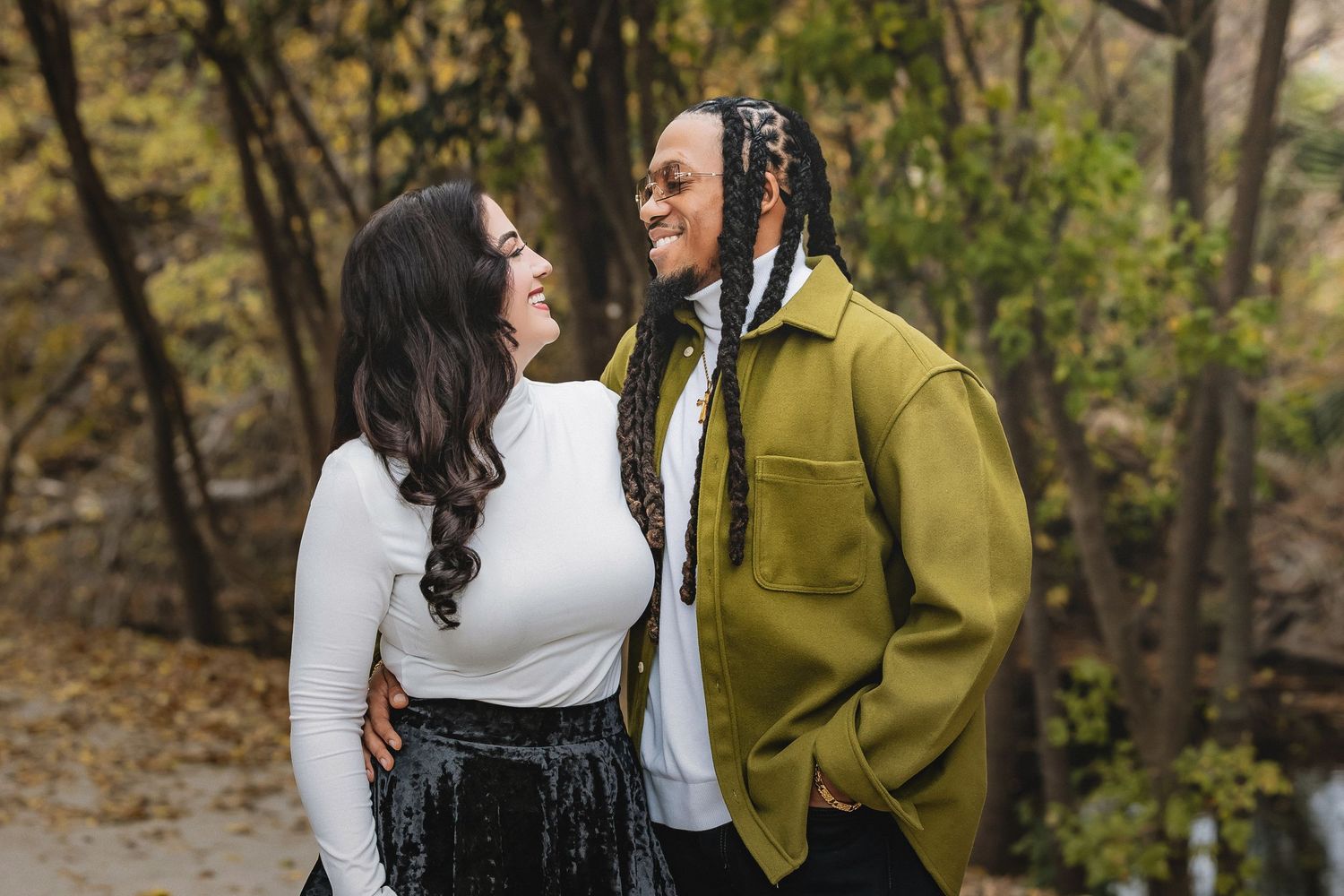 A couple in autumn attire shares a romantic moment in a wooded park setting during fall season.