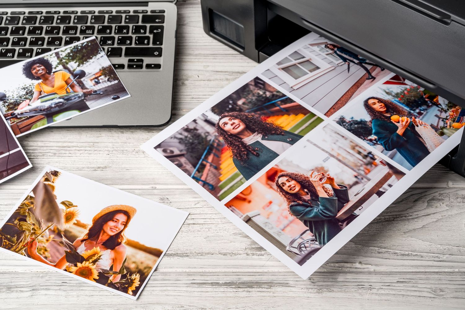 Printed photos of women coming out of a home inkjet printer on a wooden desk with a laptop nearby.