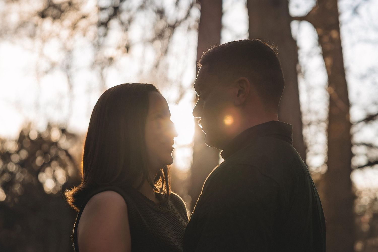 A group of people stand together in silhouette against a glowing sunset through autumn trees.