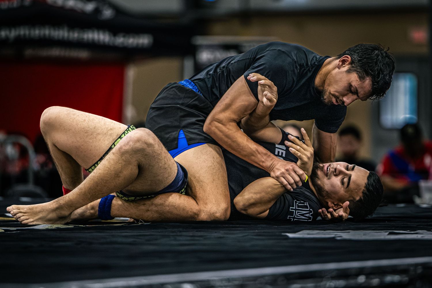 Two MMA fighters grappling on a mat during a ground training session in a martial arts gym.