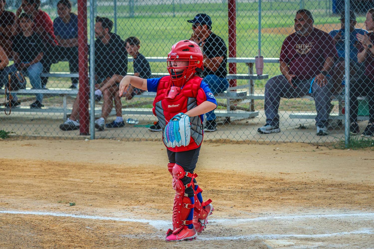 Young baseball catcher in red gear stands ready at home plate during a youth league game.