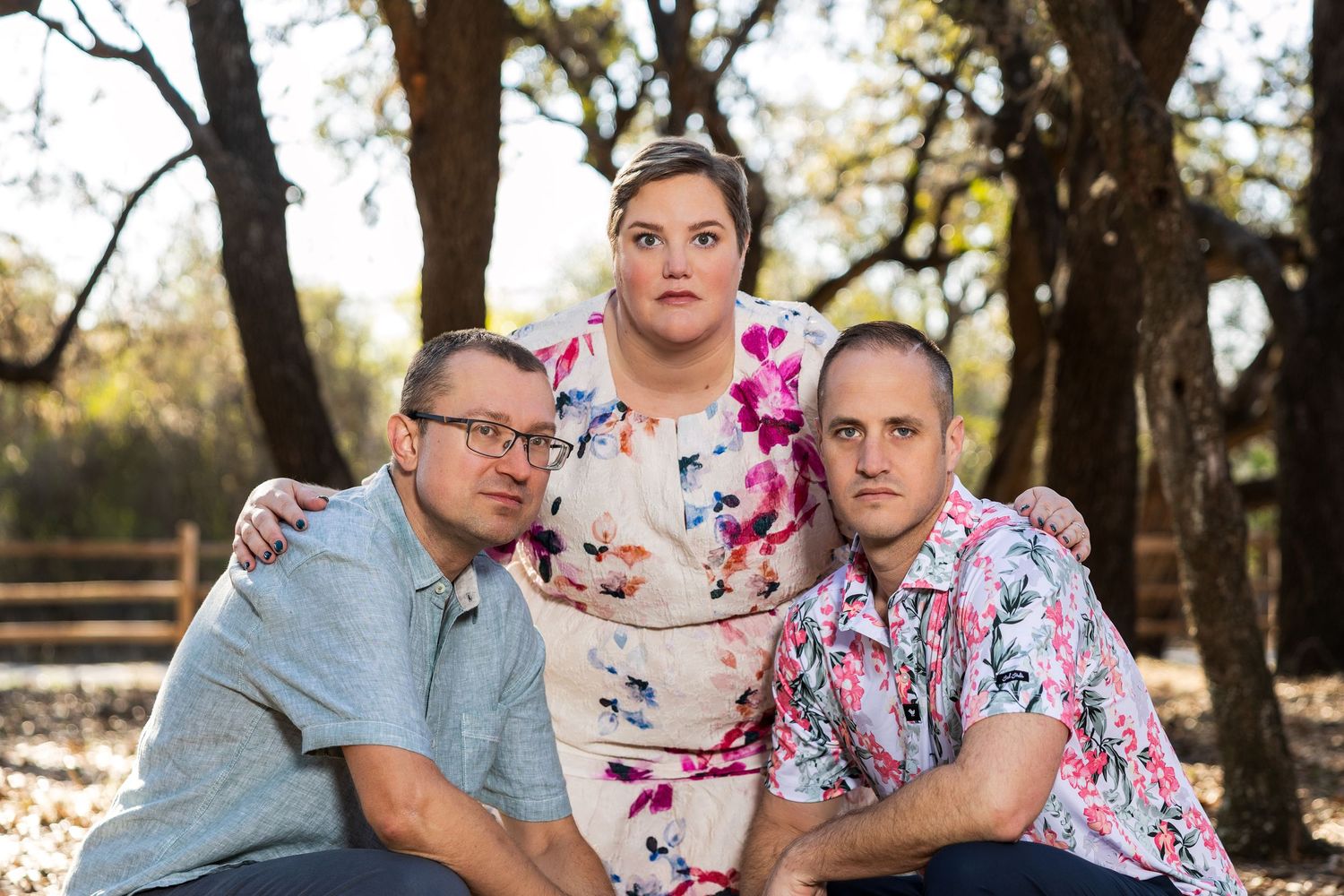 A group of three adults, two men and one woman, posing together outdoors in a natural setting.