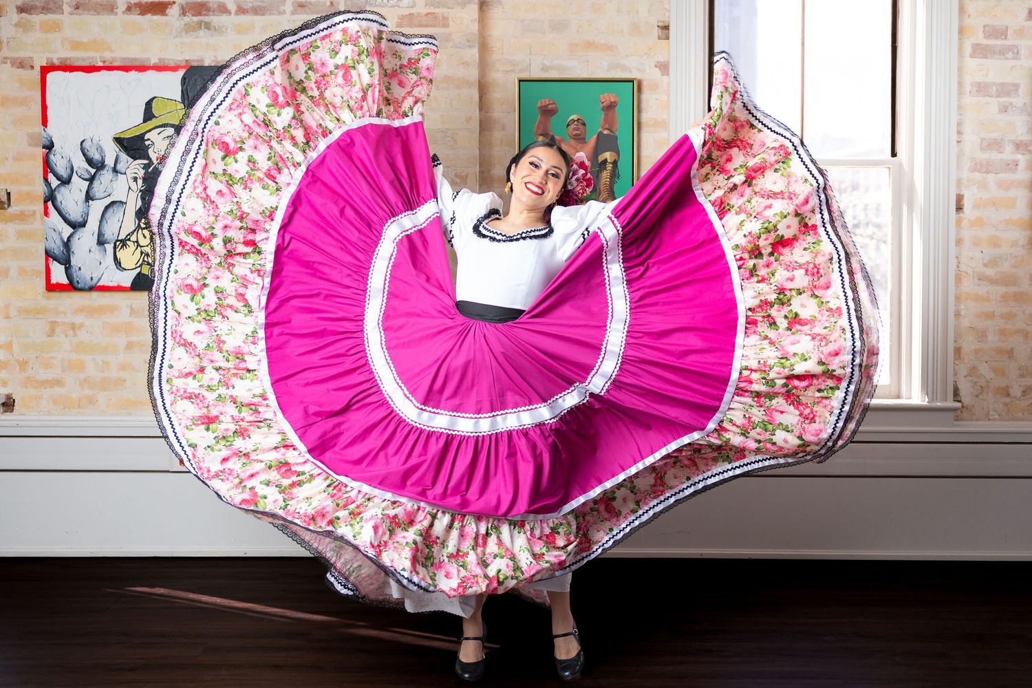A dancer in a bright pink and floral dress performs a traditional Mexican folk dance with a flowing skirt movement.