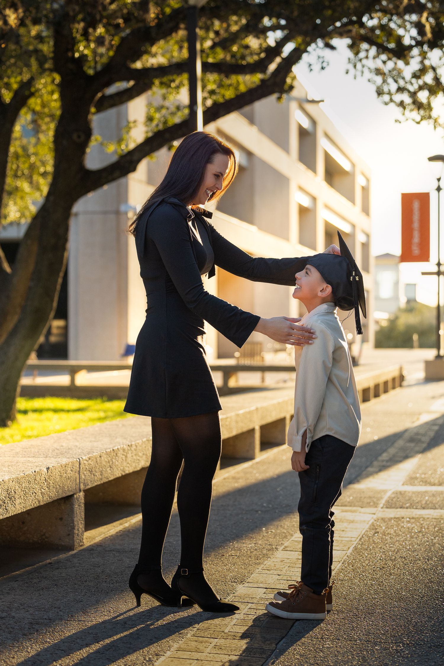 A parent and child share a tender moment together on a sunny afternoon walkway beside a building.