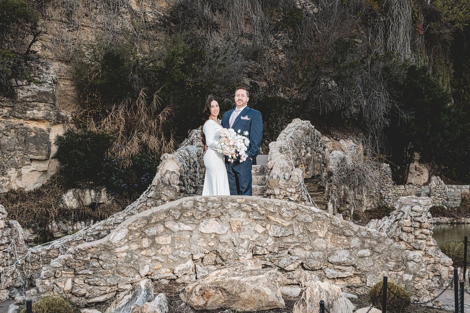 Two figures stand together on ancient stone ruins overlooking a scenic landscape during an outdoor photoshoot.
