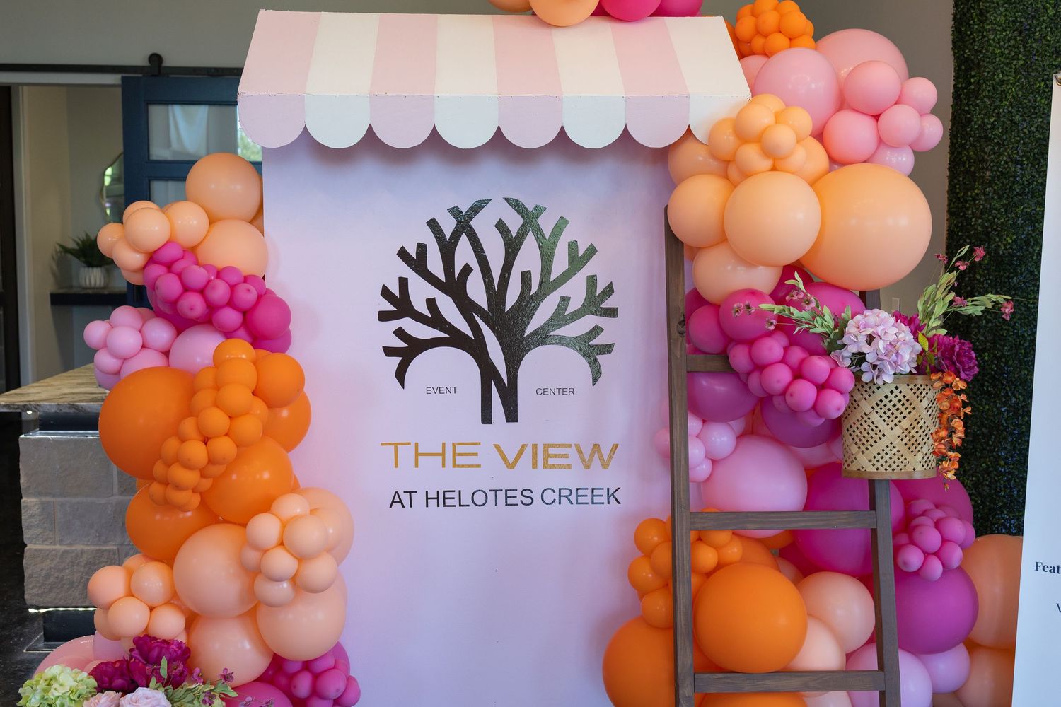 Colorful balloon arch in pink, orange decor surrounds The View at Helotes Creek sign at an outdoor event.