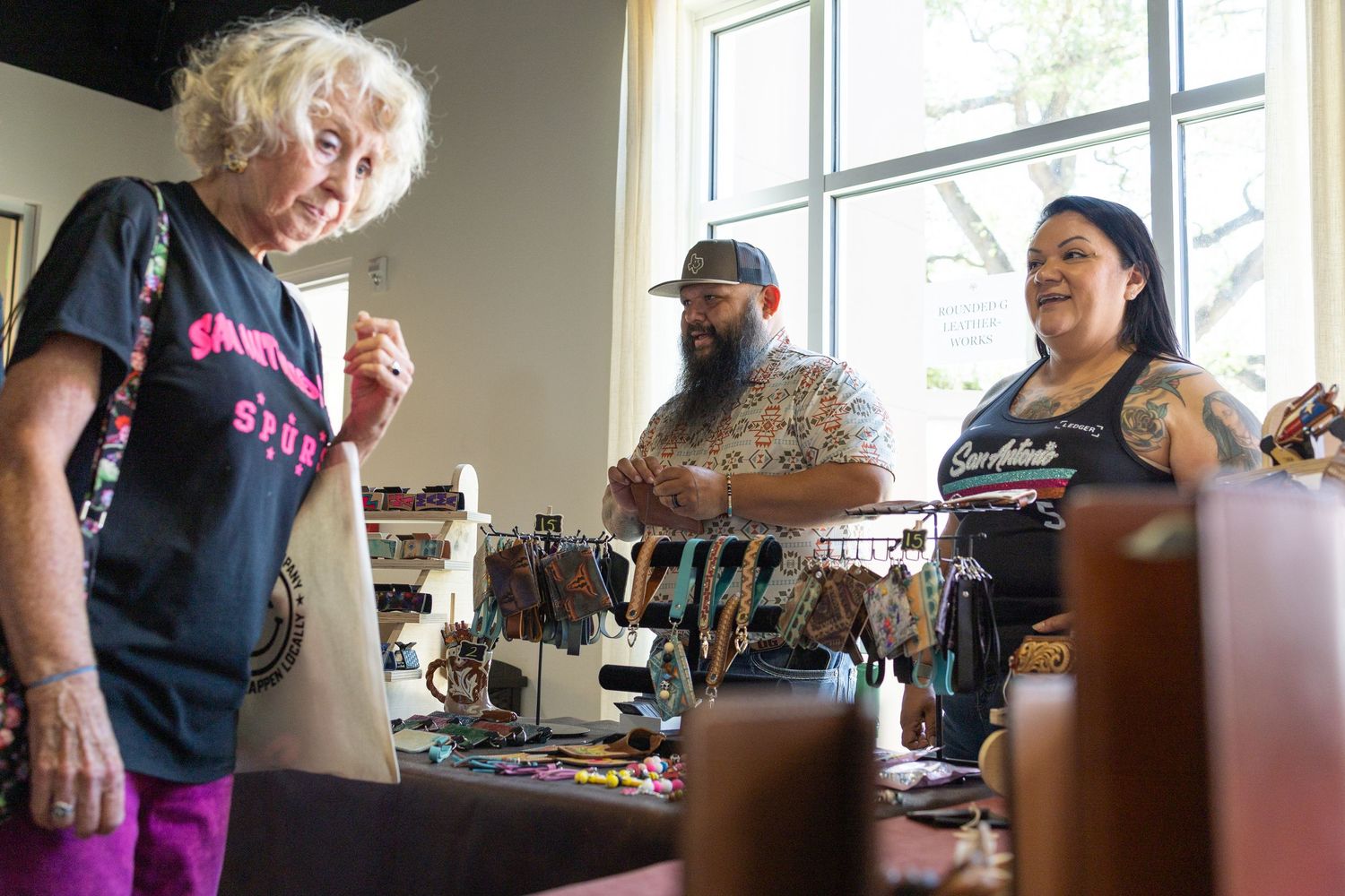 Three people browsing jewelry and accessories at an indoor retail vendor booth.