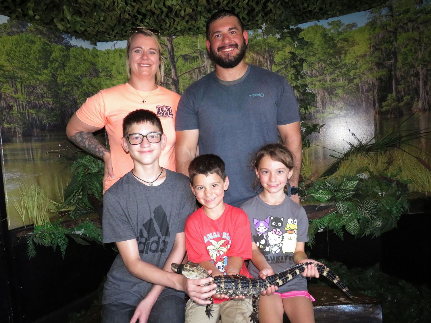 A group poses with fishing rods and caught fish at a lake during a sunny outdoor fishing excursion.