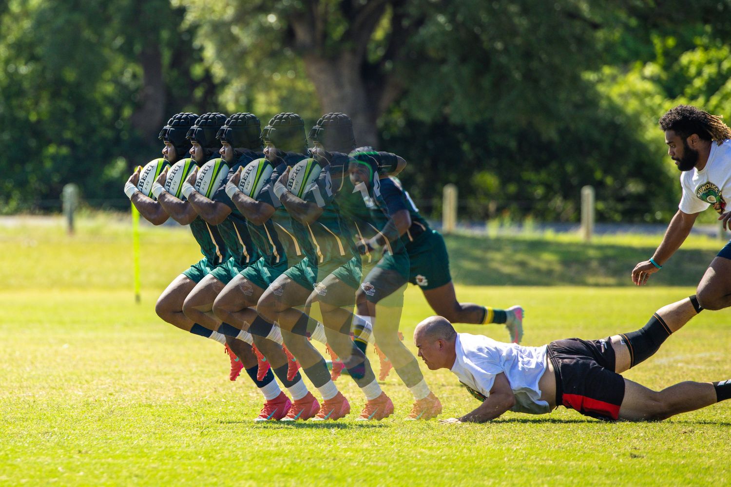 Rugby players line up in formation during a match, with a player diving to tackle on a sunny green field.