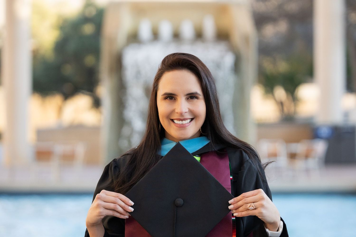 A group of people pose together outdoors wearing black graduation caps and gowns during a commencement ceremony.