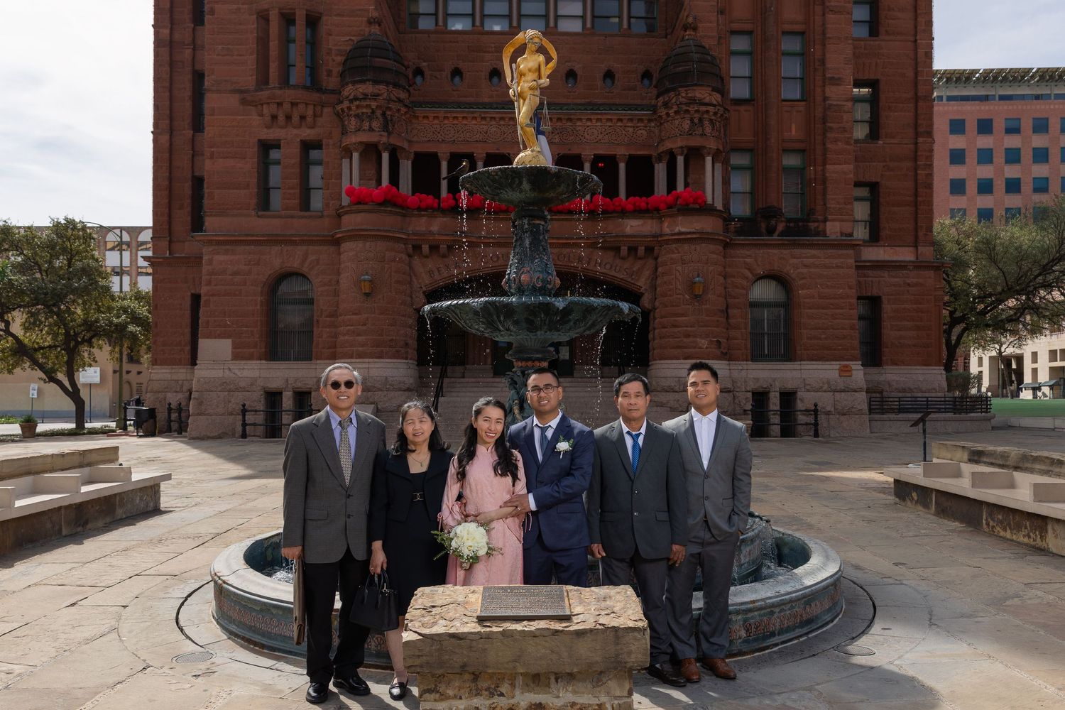 A group stands near a historic brick courthouse building with a decorative fountain in the foreground.