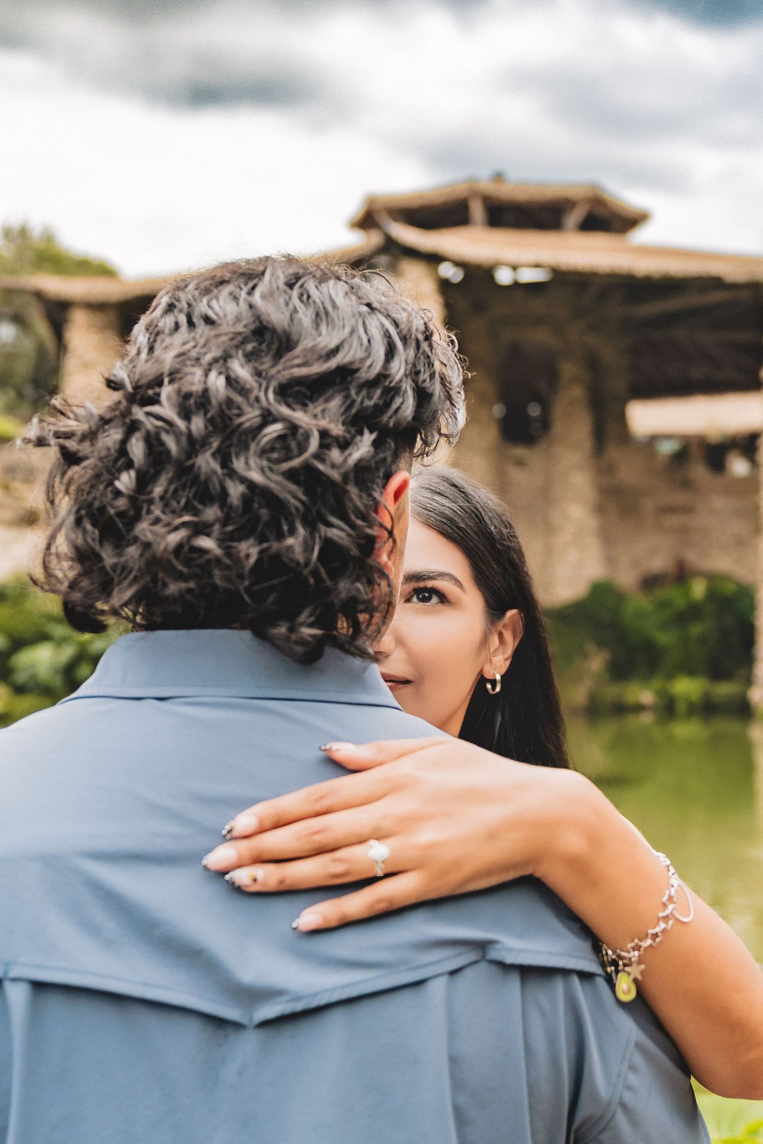 Woman embracing man from behind during romantic outdoor engagement photo session.