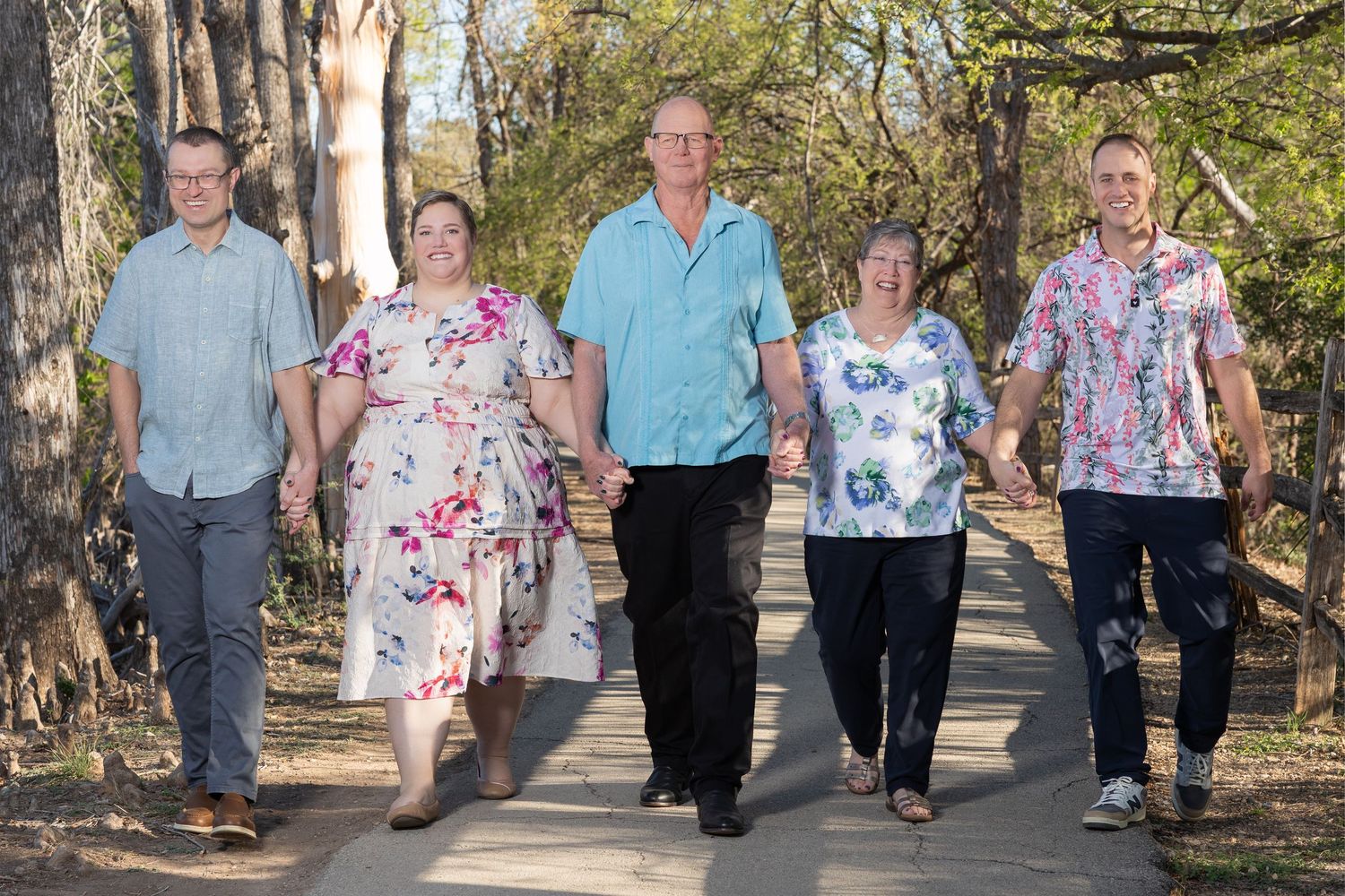 A group of five adults, two men and three women, walking together on a path through a wooded area.