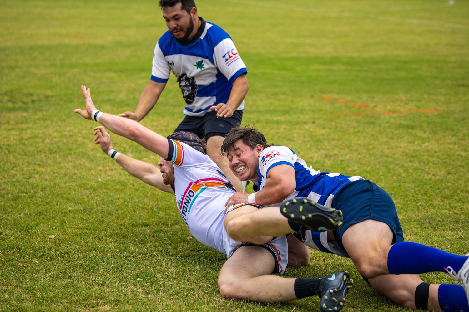 Rugby player tackled to the ground during an intense match on a green grass field.