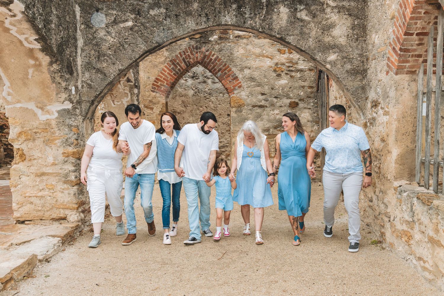 Family group walking together under a historic stone arch at Mission San Juan Capistrano on a sunny day.