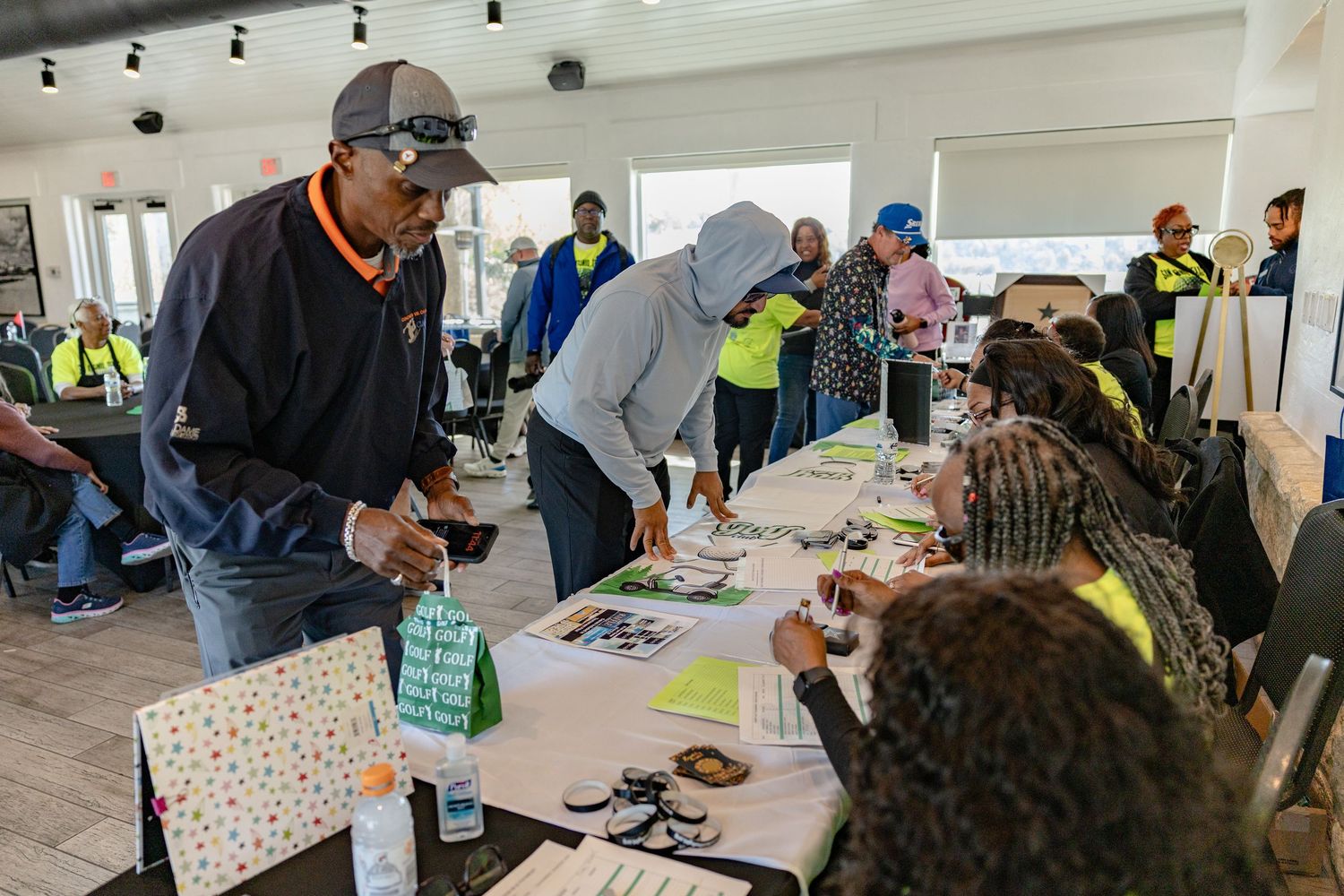 People signing in at a registration table during a community event in a bright indoor venue with attendees in safety vests.