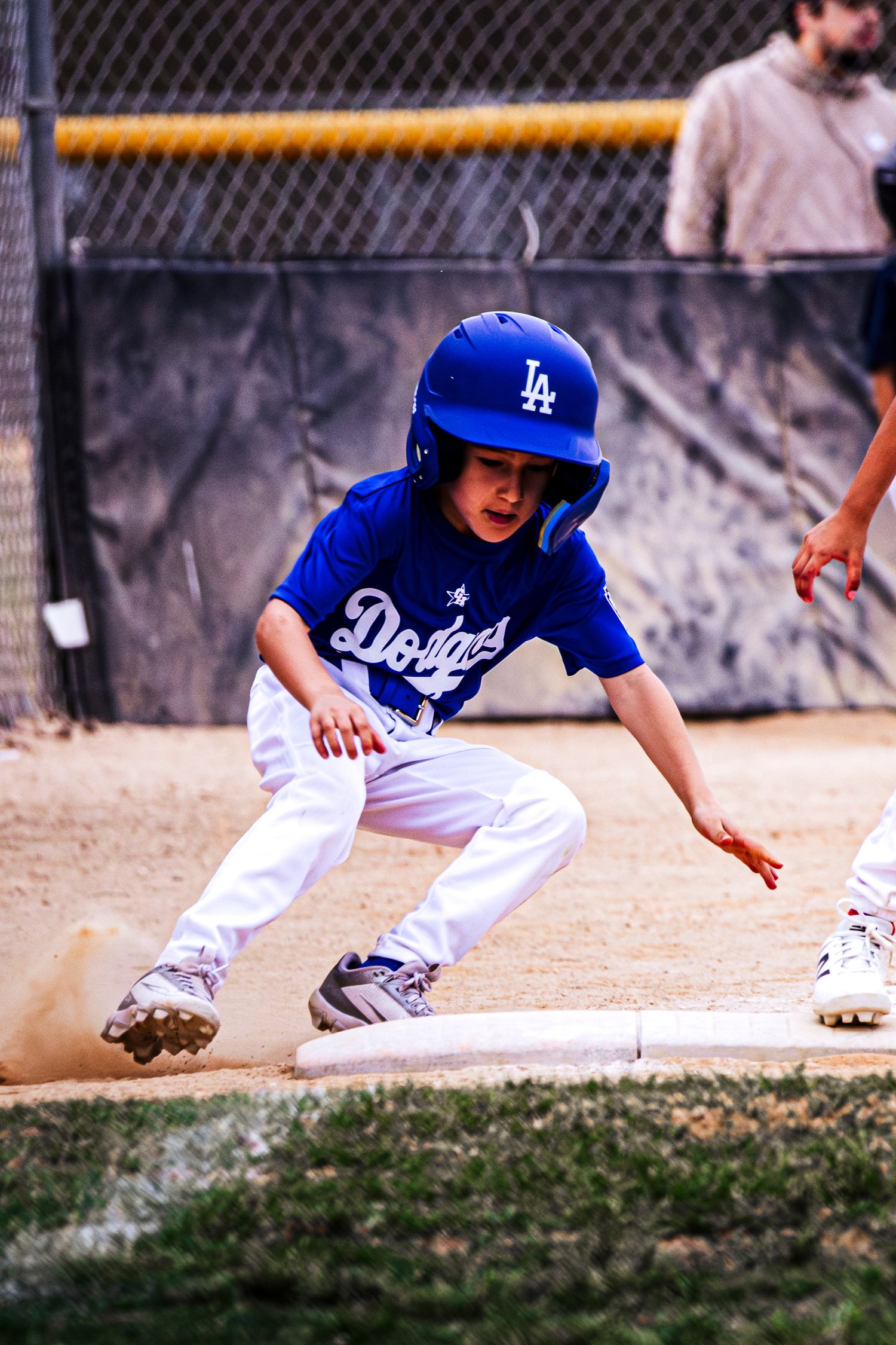 Young boy in LA Dodgers uniform sliding into base during little league baseball game.